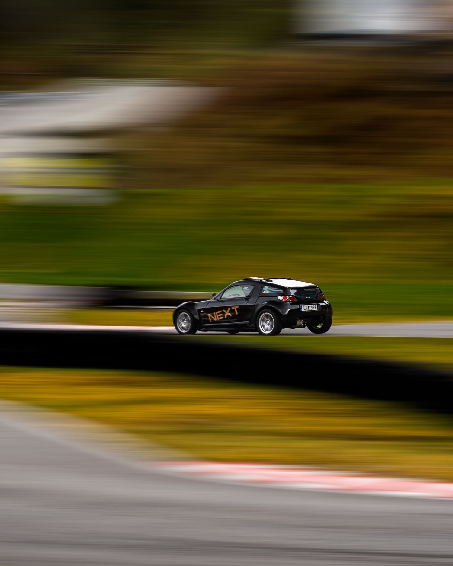 Black race car speeds past on a racetrack with motion blur effect creating a dynamic sense of movement.