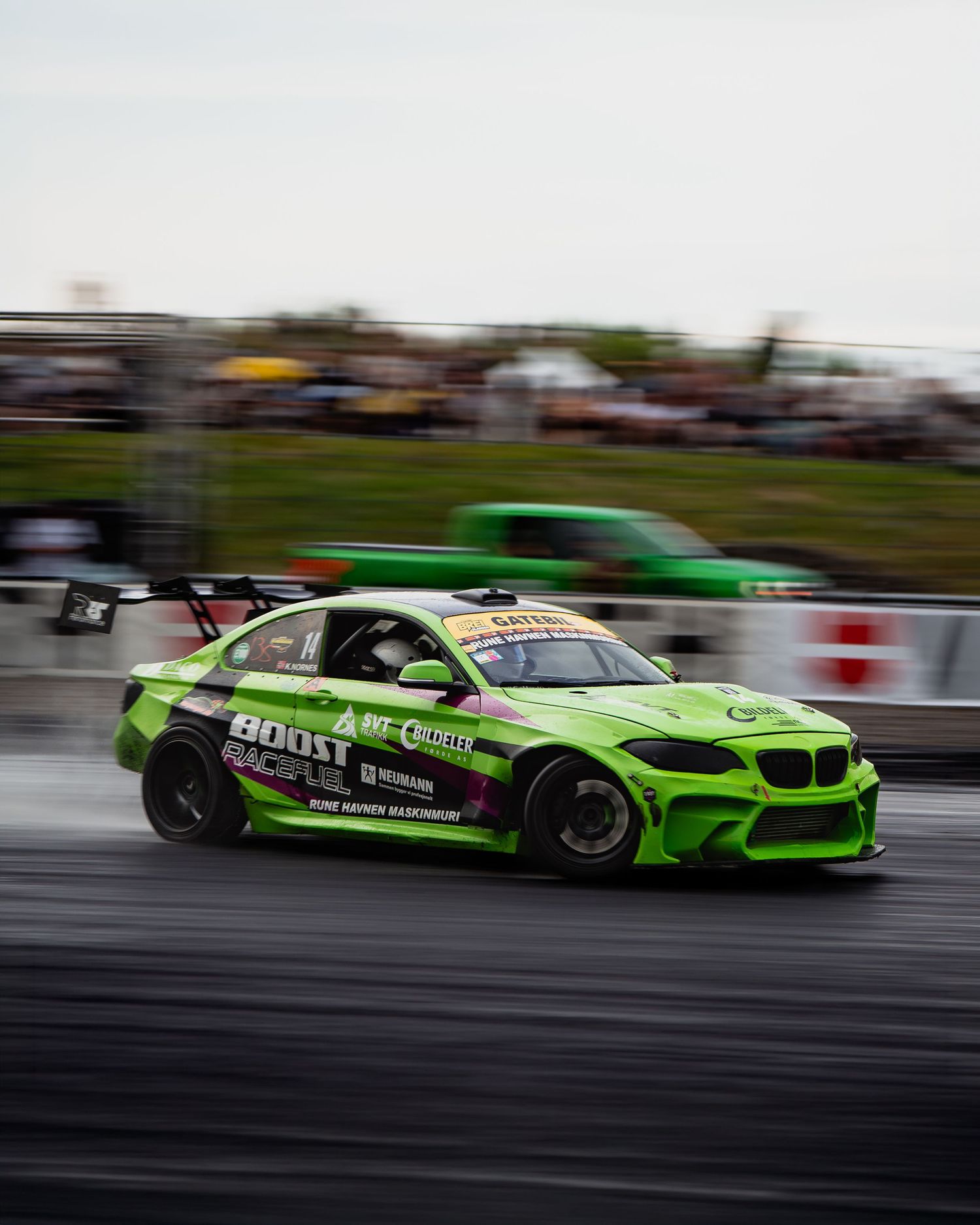 Bright green BMW drift car racing sideways on track with motion blur effect showing high speed performance.