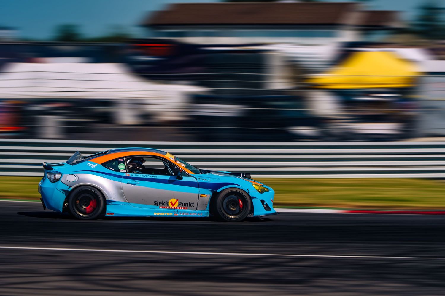 Light blue sports car racing at high speed on a racetrack with motion blur and red accented wheels.