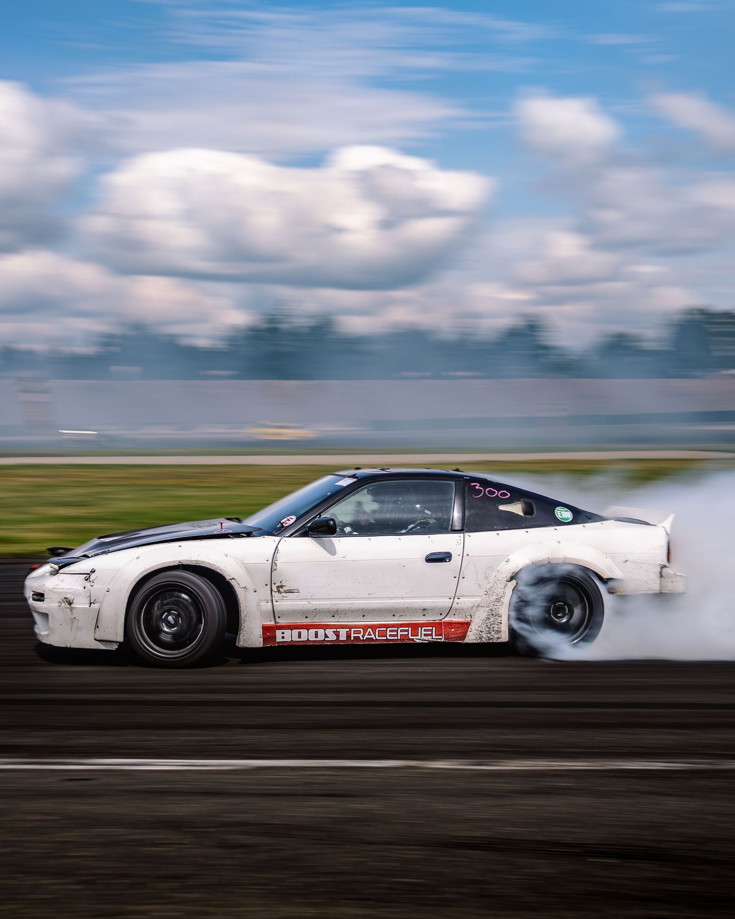 White drift car racing sideways on track with dramatic cloudy sky in motion blur effect.