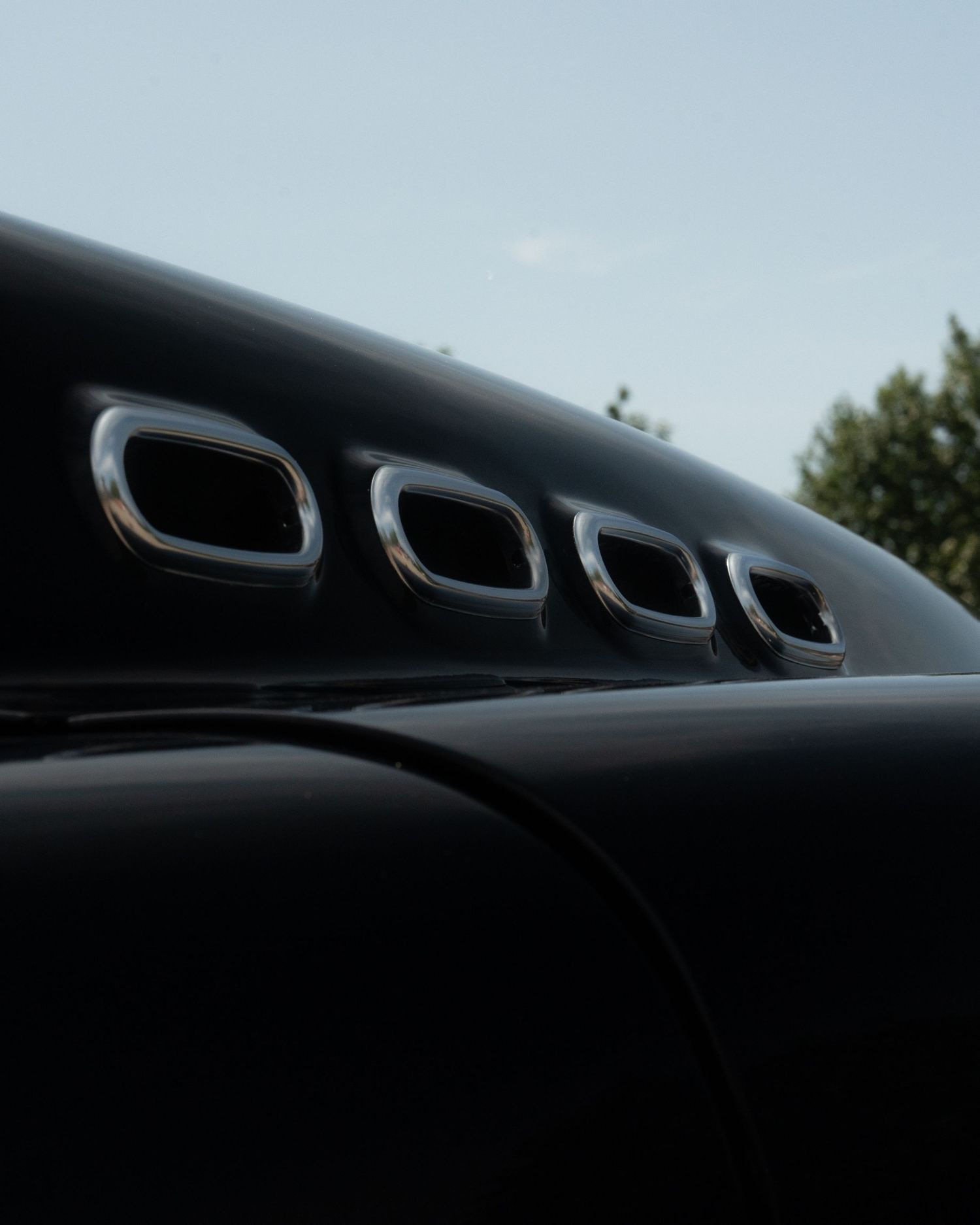 Close-up silhouette of classic car hood vents against a light blue sky.