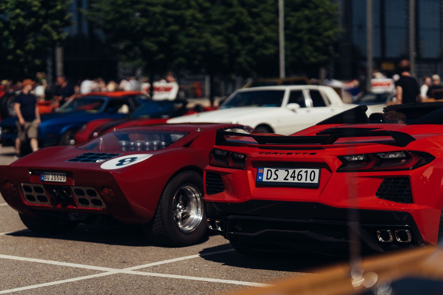 Red sports cars lined up at an outdoor car show with spectators in background.