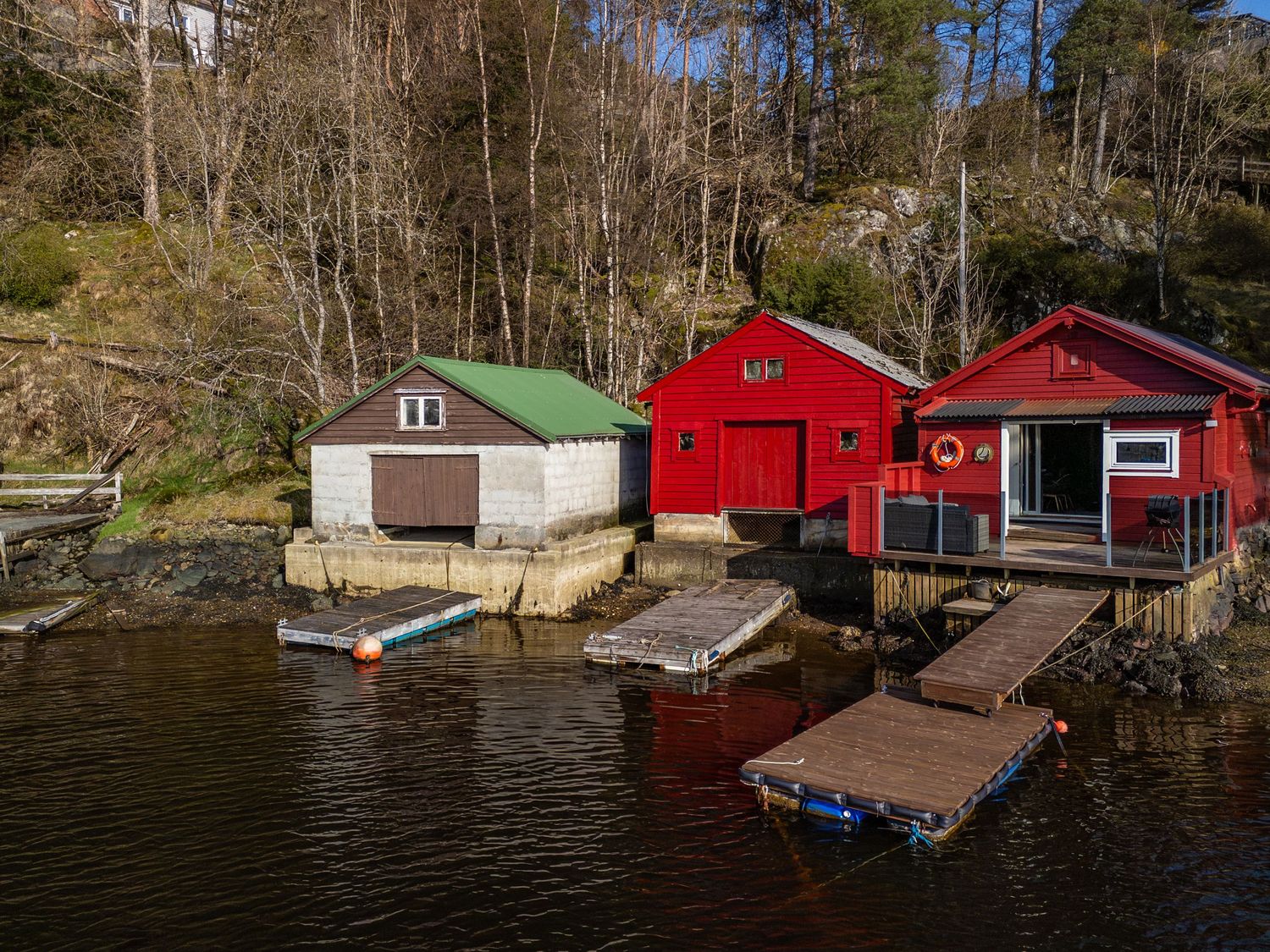 Row of colorful boathouses with floating docks built along the rocky Norwegian coastline.