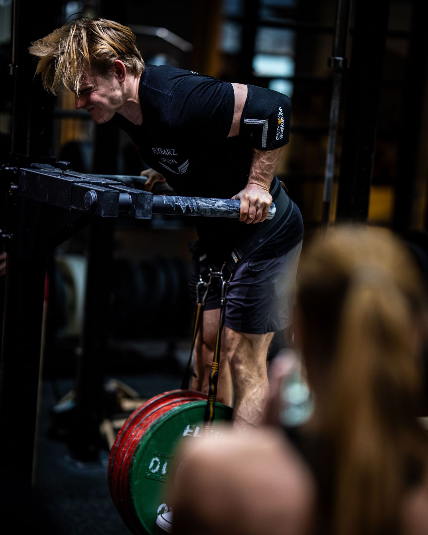 Side view of athlete performing chest-supported exercise on parallel bars with weight plates below.