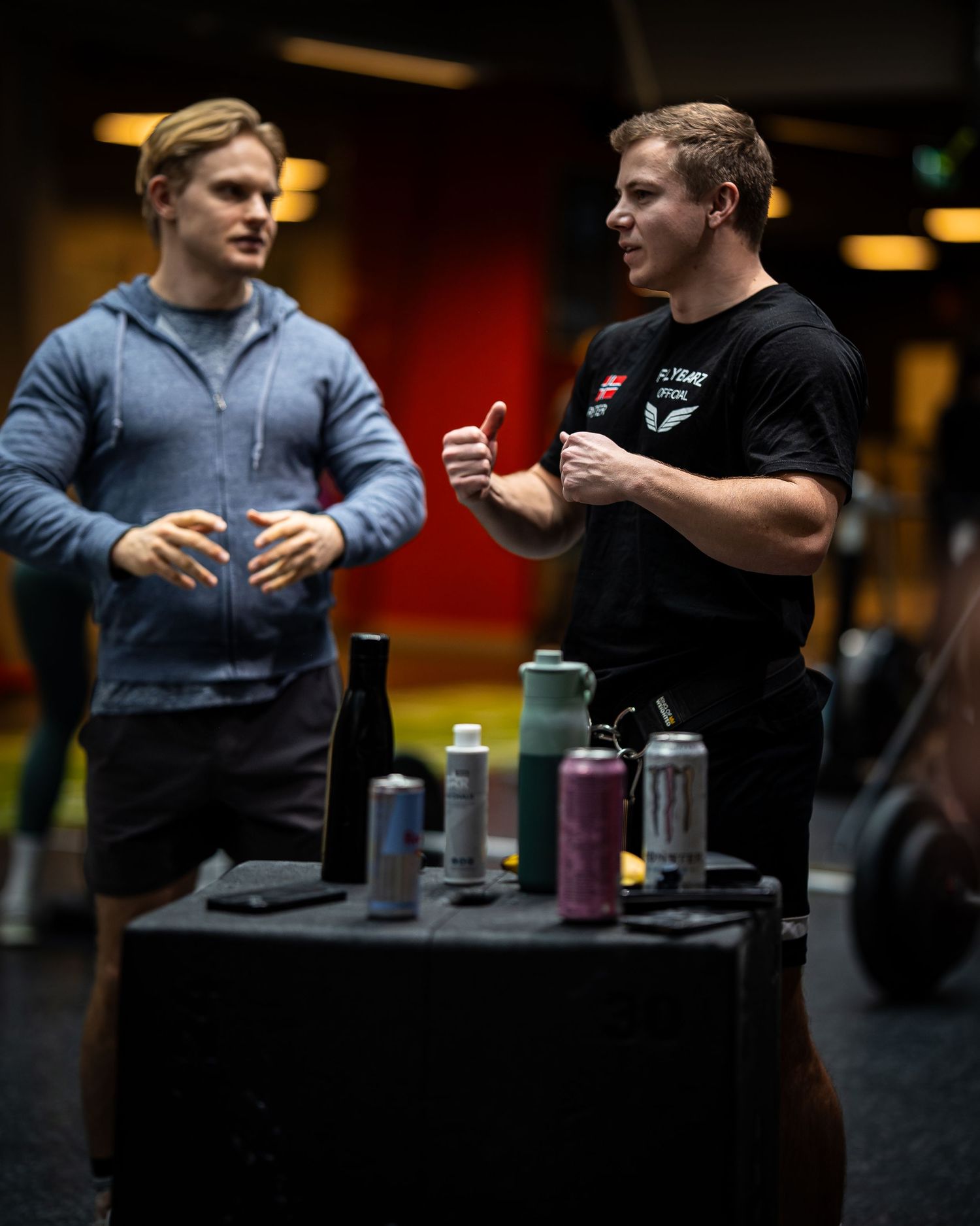 Two people having conversation near table with drinks in fitness facility.