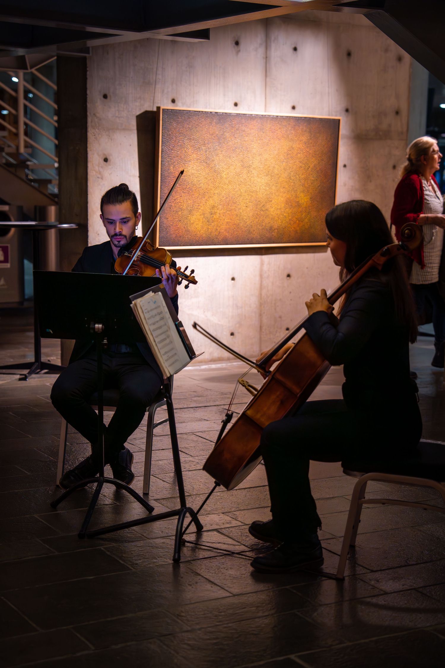String quartet musicians perform in front of illuminated artwork in a dimly lit venue.