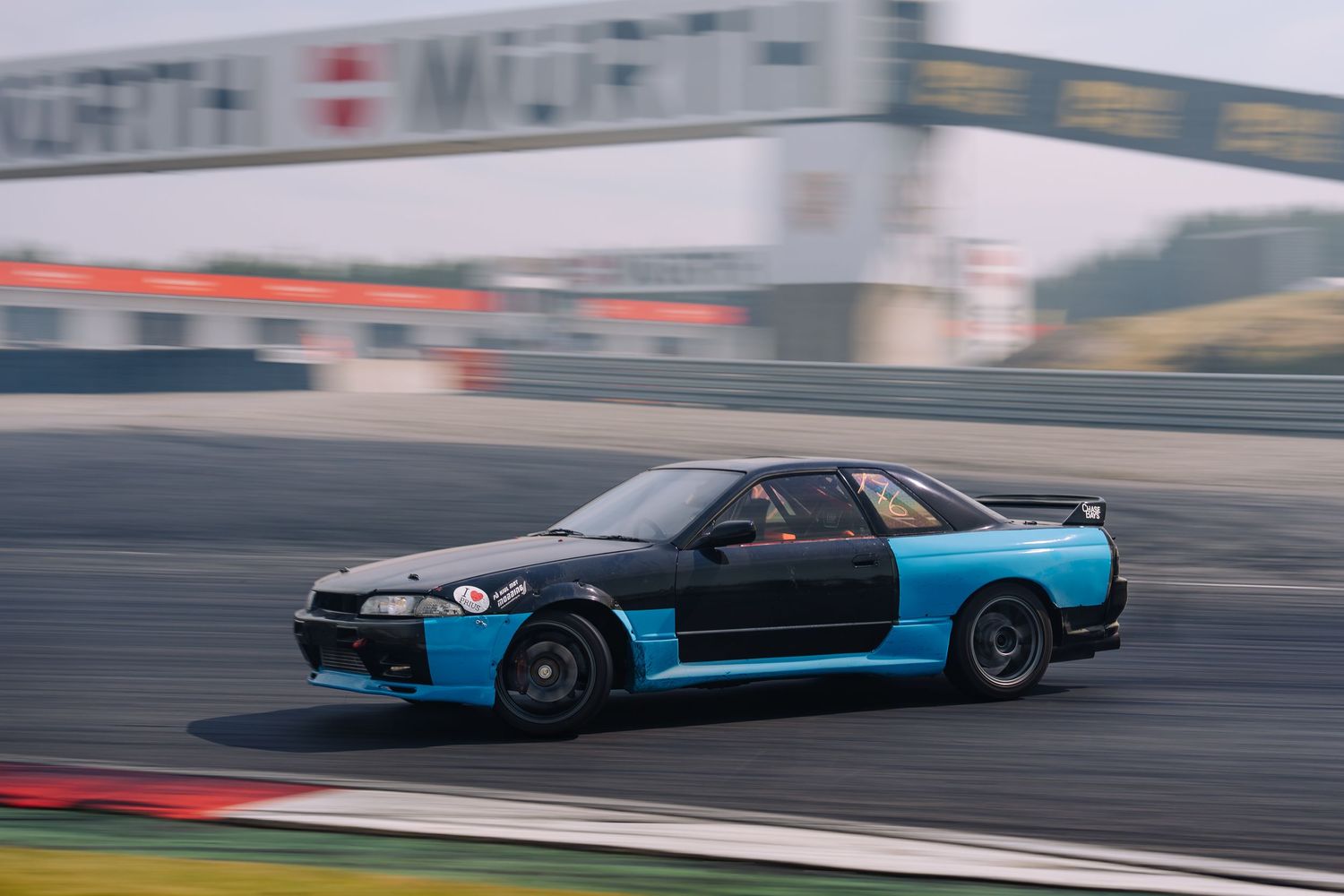 A black and blue Nissan Skyline GT-R drifting on a racetrack with motion blur.
