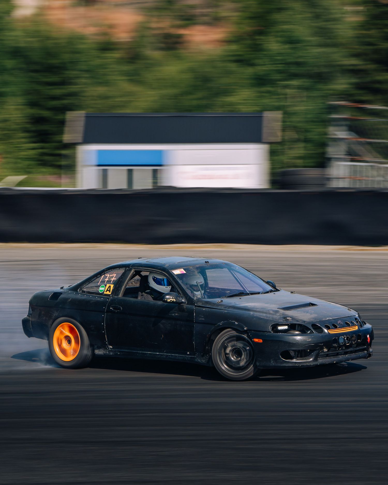 A black drift car sliding sideways with glowing brake rotors on a racetrack at dusk.