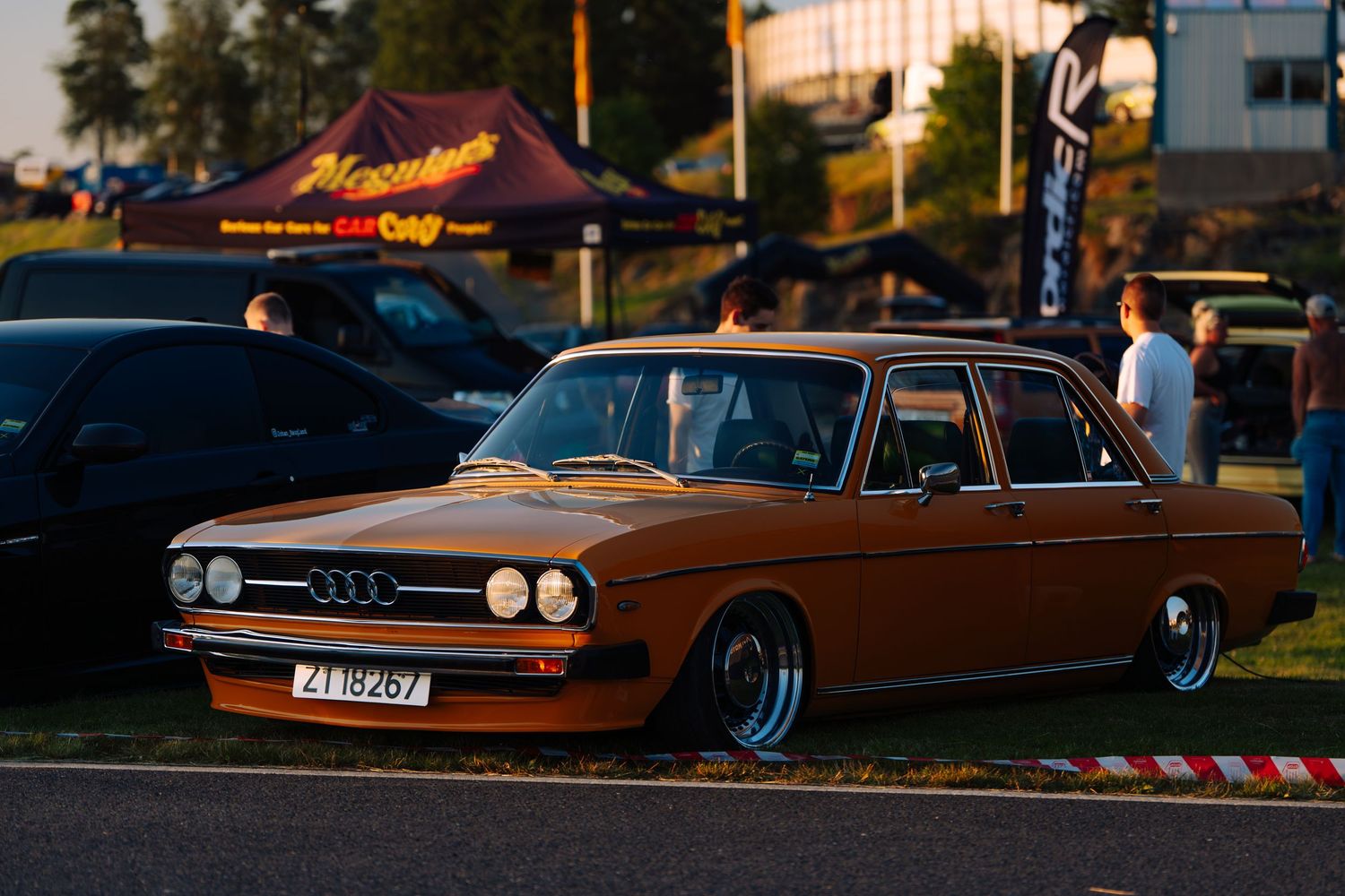 A row of vintage Audi cars lined up at sunset during a car show or meetup event.