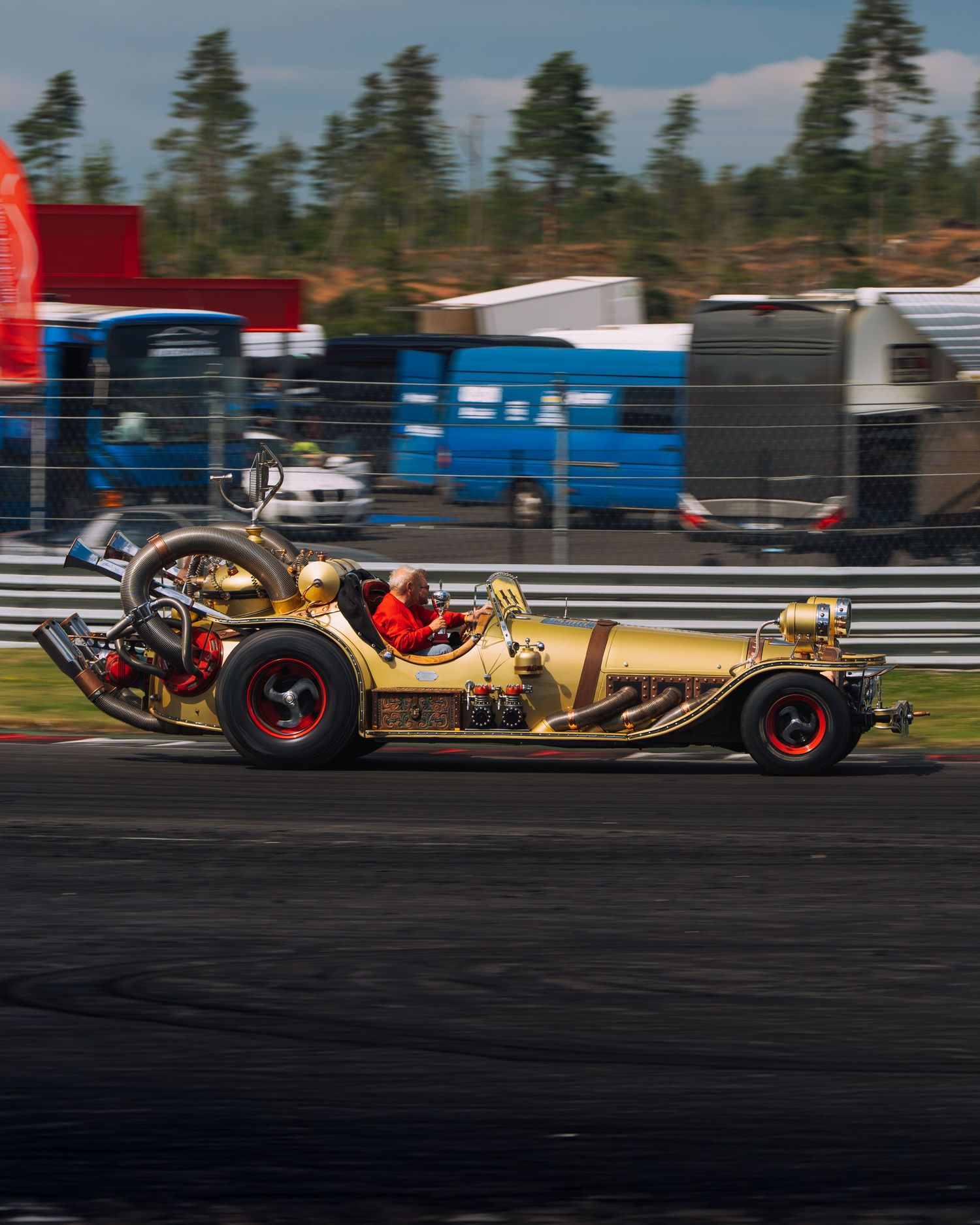 Gold vintage racing car with exposed engine and large rear tires speeds along racetrack during competition.