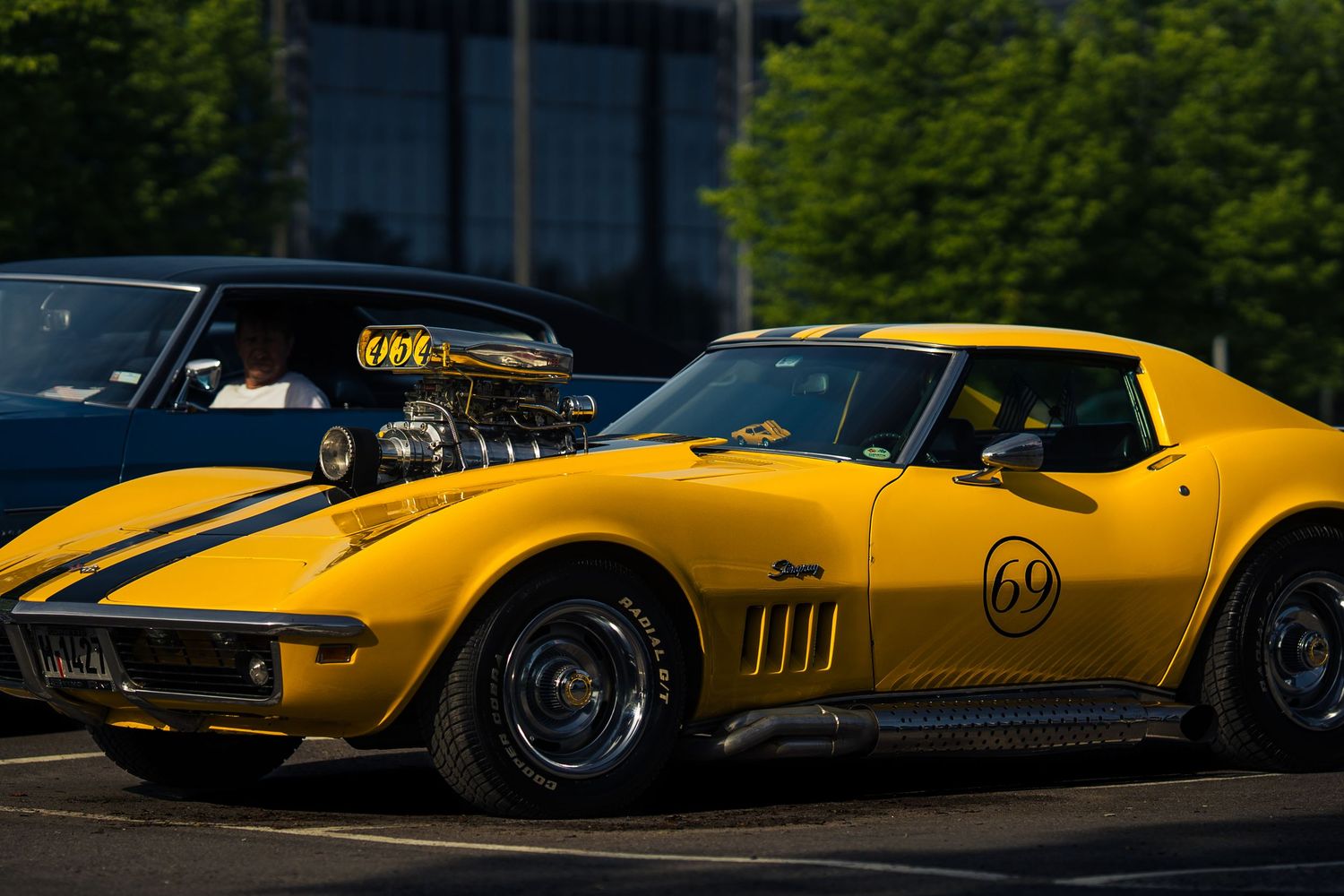 Yellow Chevrolet Corvette with racing stripes parked in outdoor lighting.