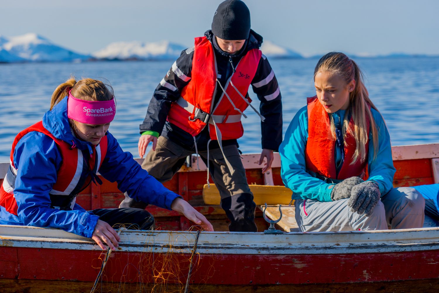 Small wooden boat with passengers in safety vests navigate cold Nordic waters.