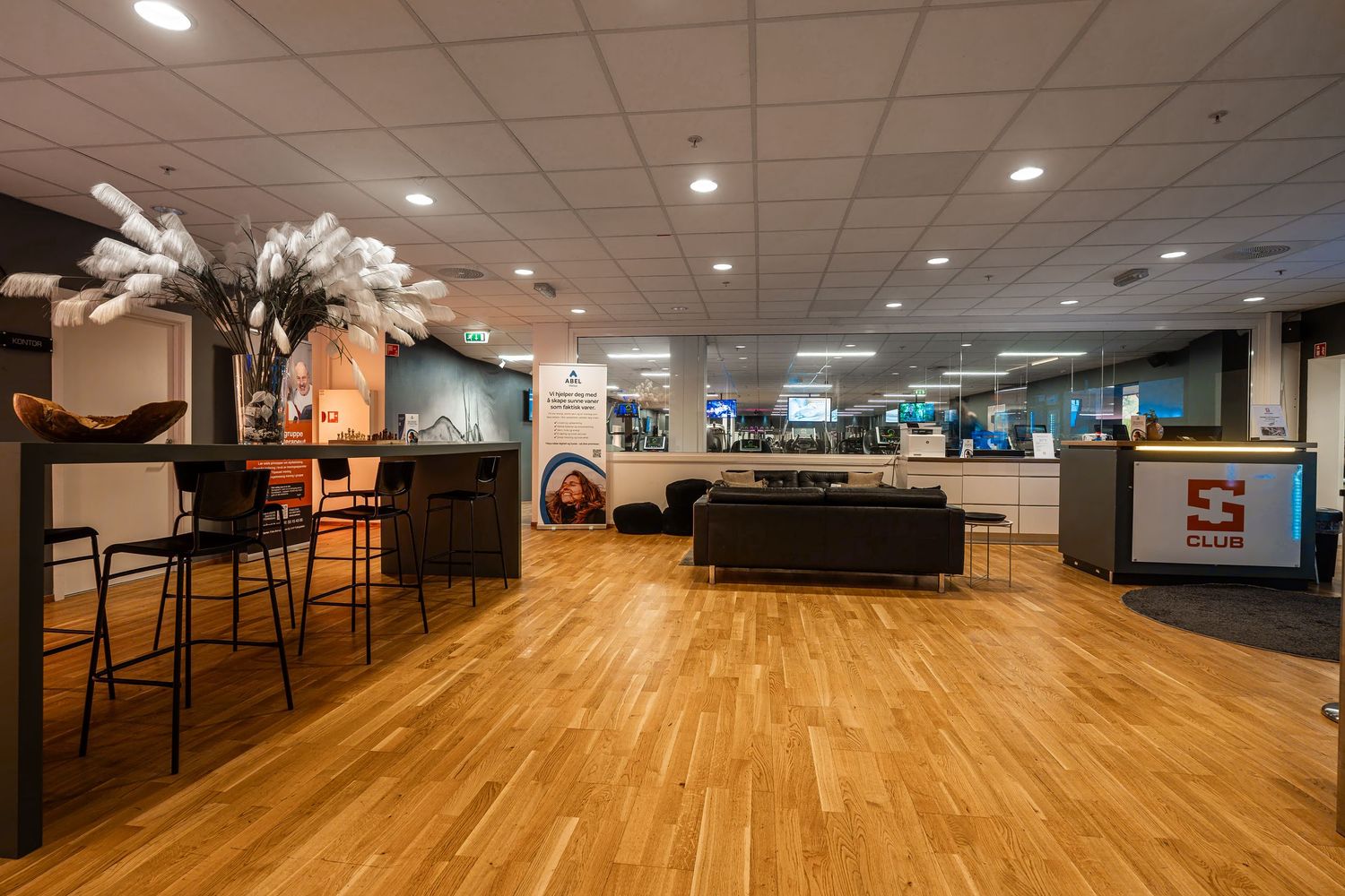 Open concept lounge with wooden floors, bar seating, and entertainment screens in background.