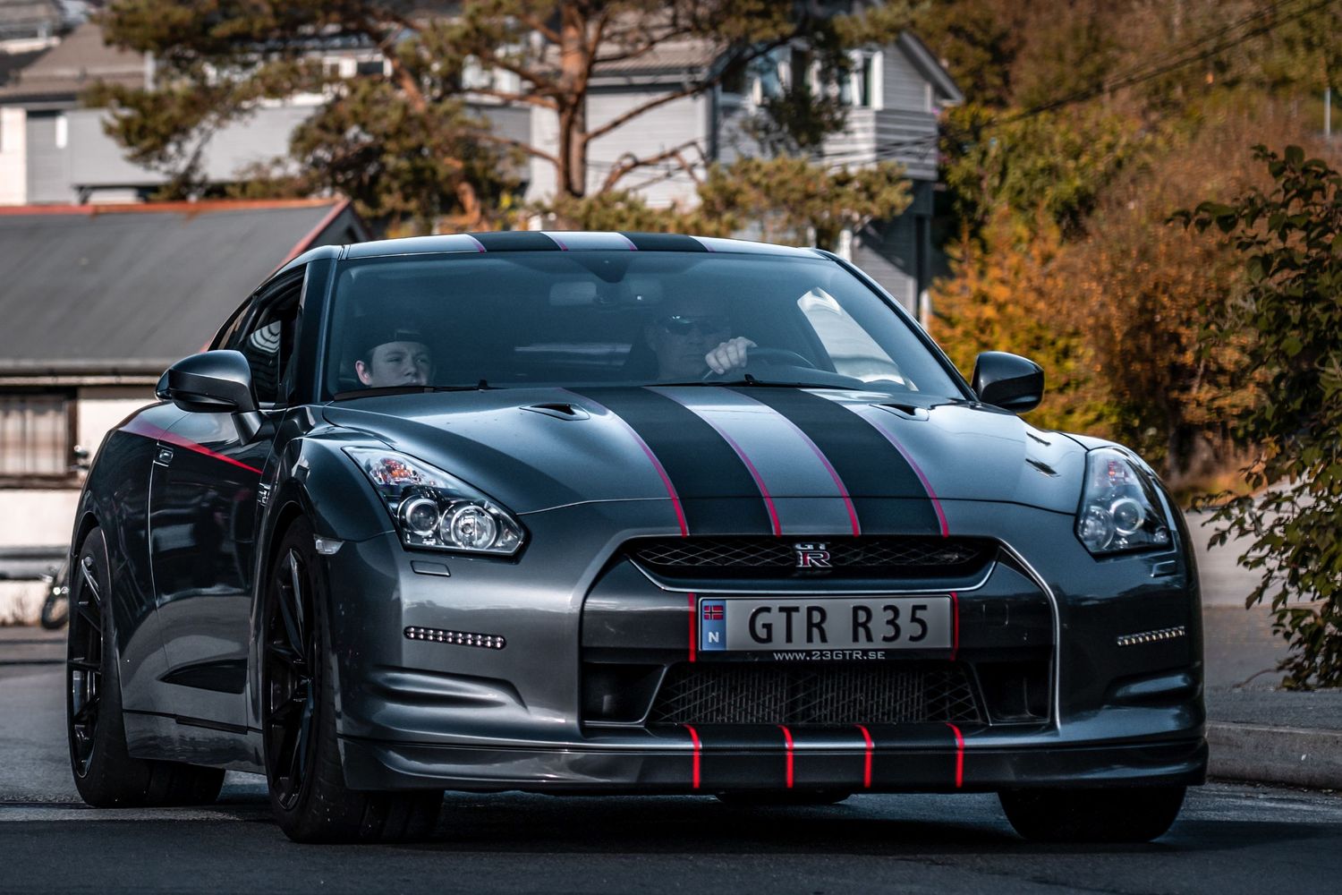 Dark blue Nissan GT-R with racing stripes parked on street during autumn.