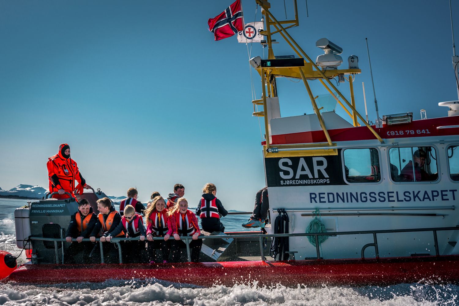 Norwegian rescue vessel with crew members conducting maritime operations in fjord waters.