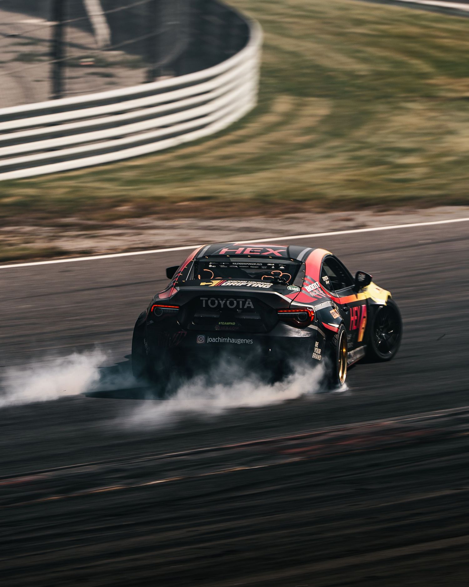 A Toyota race car drifts around a track corner with smoke billowing from its tires during a motorsport competition.