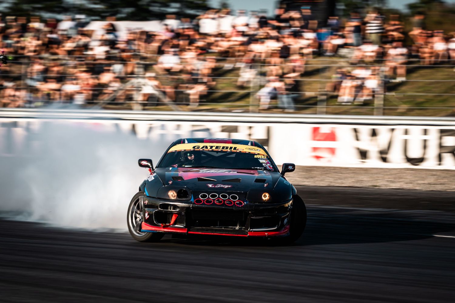 Red sports car drifting on racetrack with smoke trailing behind during competitive motorsport event.