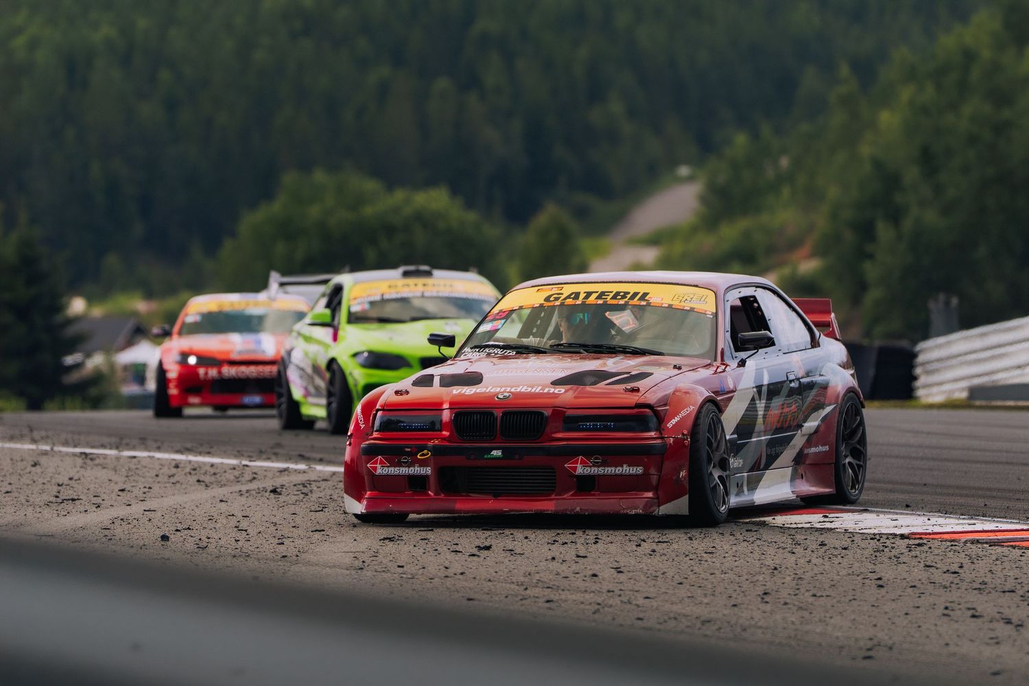 A row of red racing cars lined up on a dirt track during a demolition derby competition.