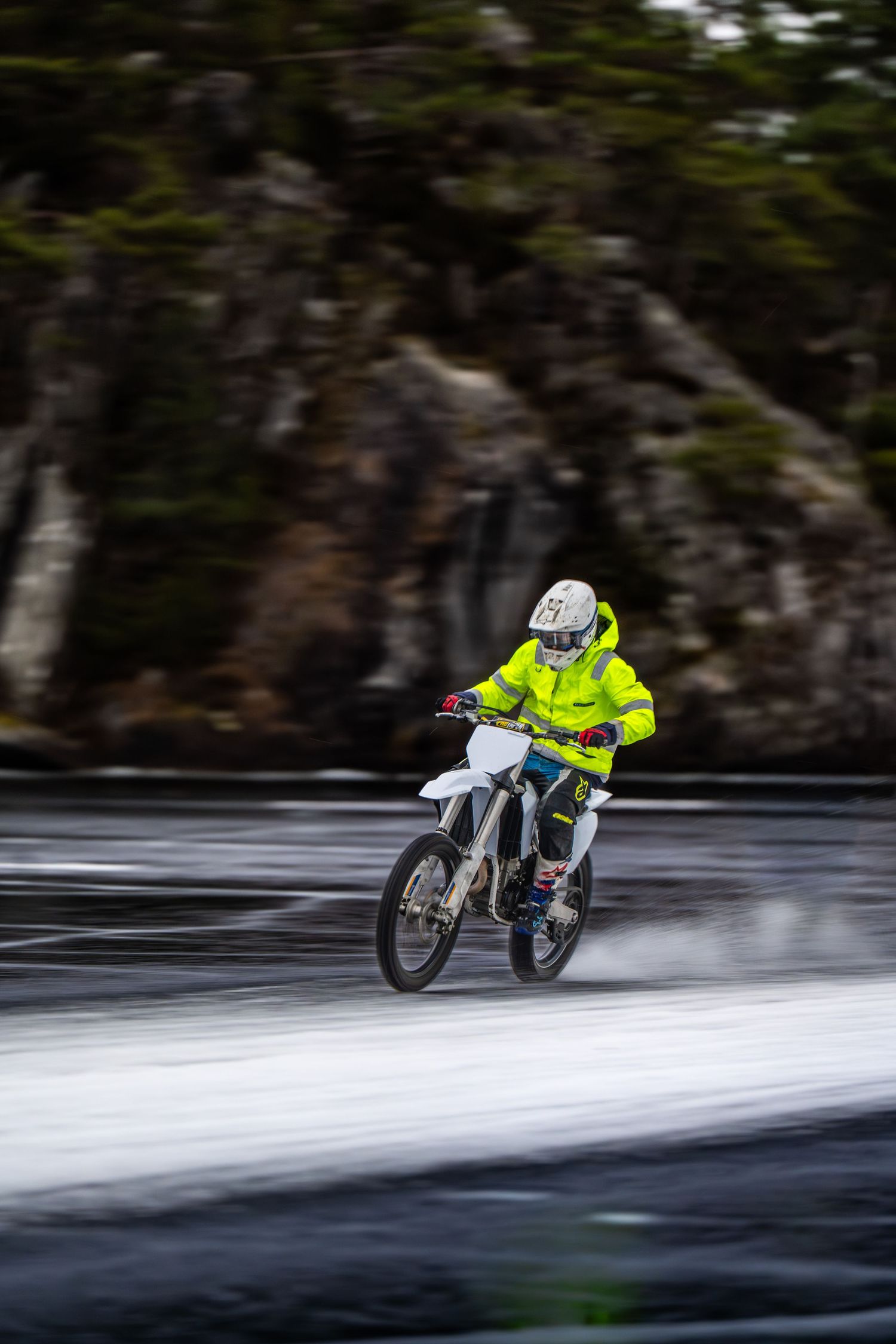 A motorcyclist in bright yellow safety gear performs a daring water crossing on a dirt bike, creating dramatic splashes.