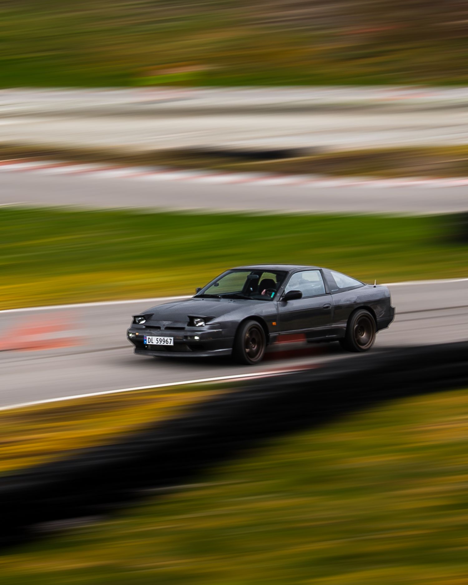 Motion-blurred black sports car speeding on a racetrack with green and yellow background.