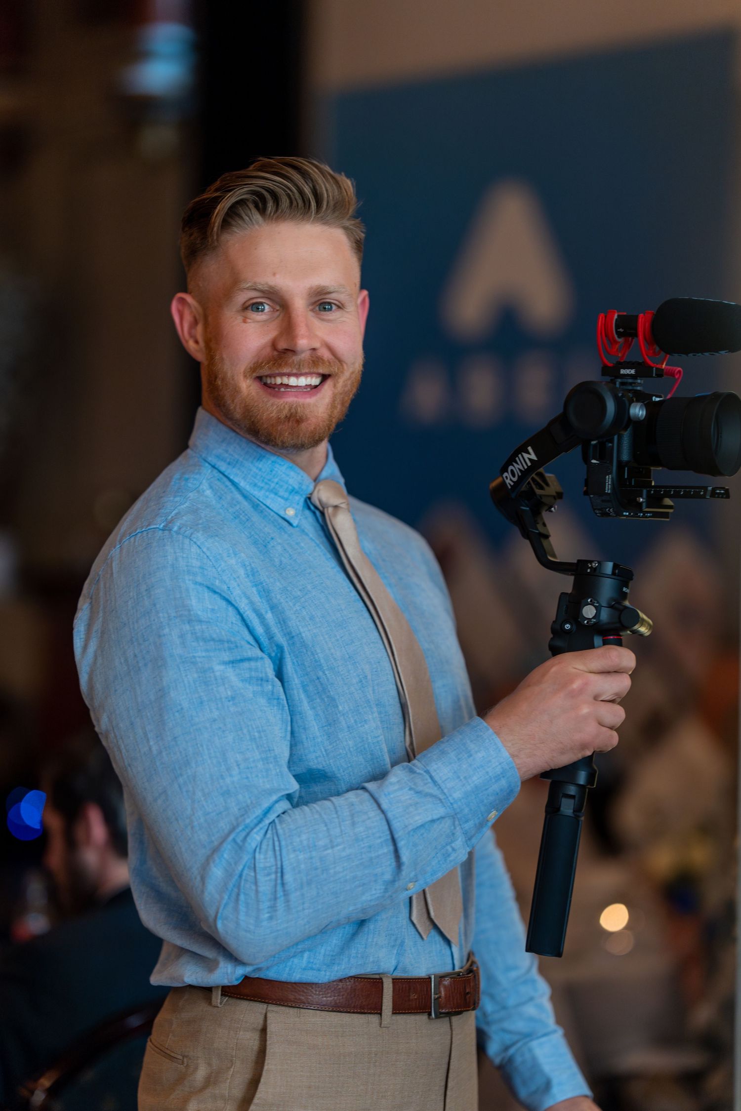 Videographer in light blue shirt filming event with professional camera equipment.