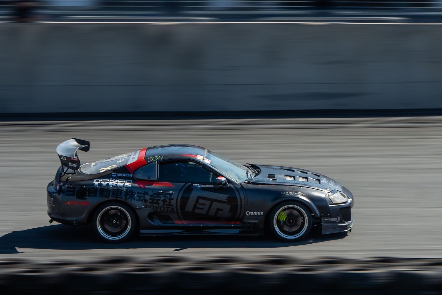 Race cars speed around a track during a high-performance motorsport competition event.