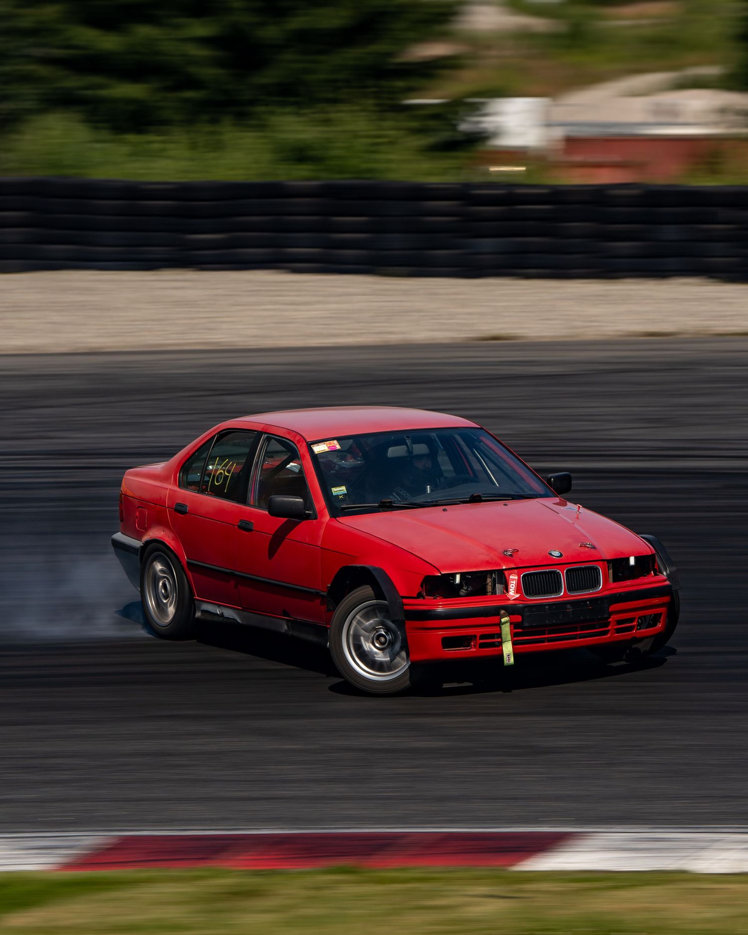 Red BMW drifting on a racetrack with tire smoke trailing behind in dramatic motion.