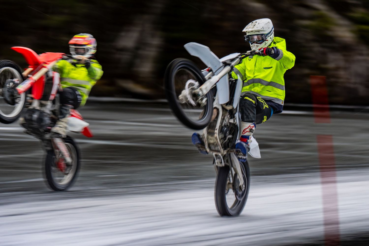 Motorcyclist performing a wheelie on a street while wearing high-visibility safety gear.