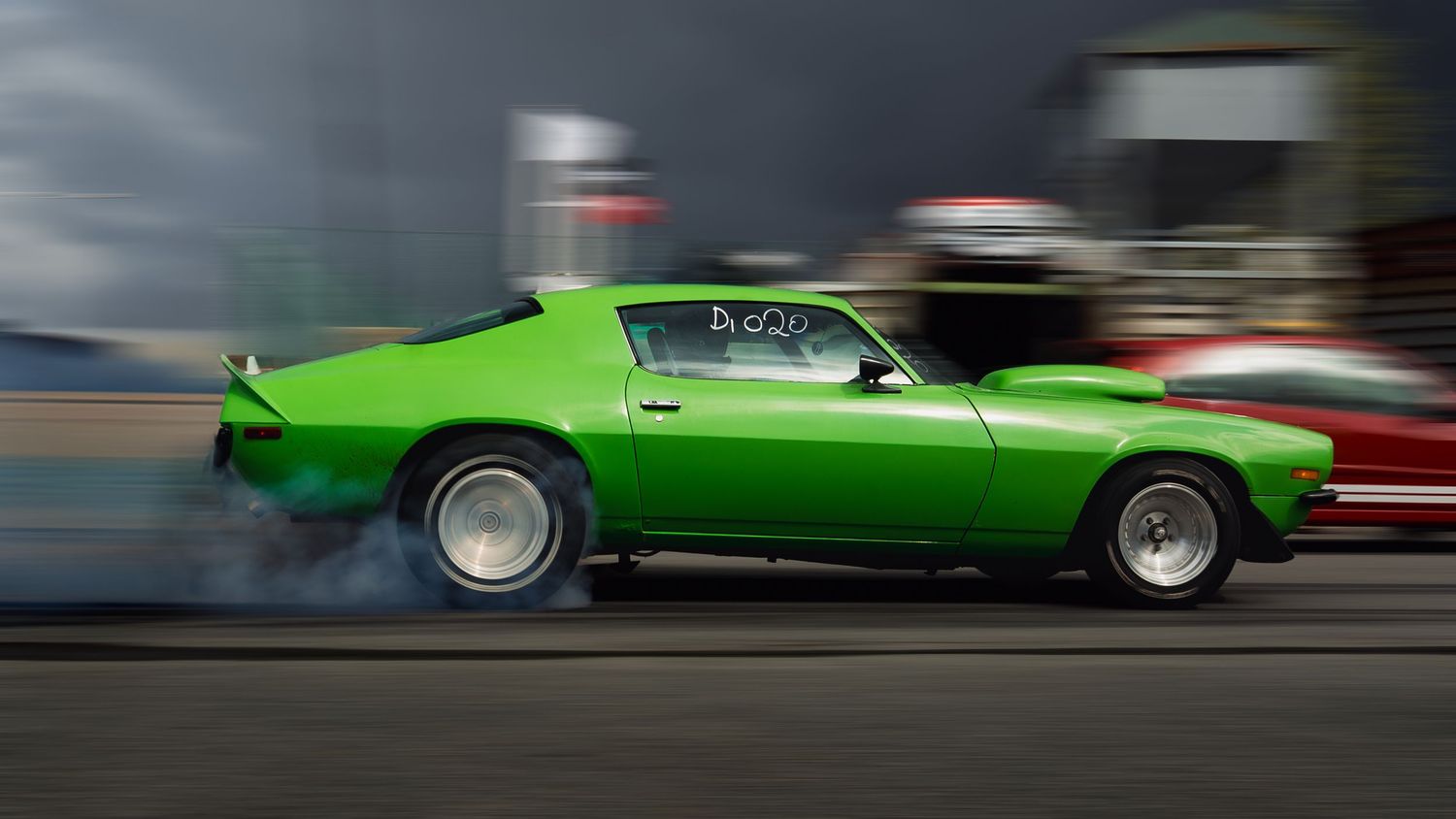 Green vintage car racing on track captured with dramatic motion blur effect.