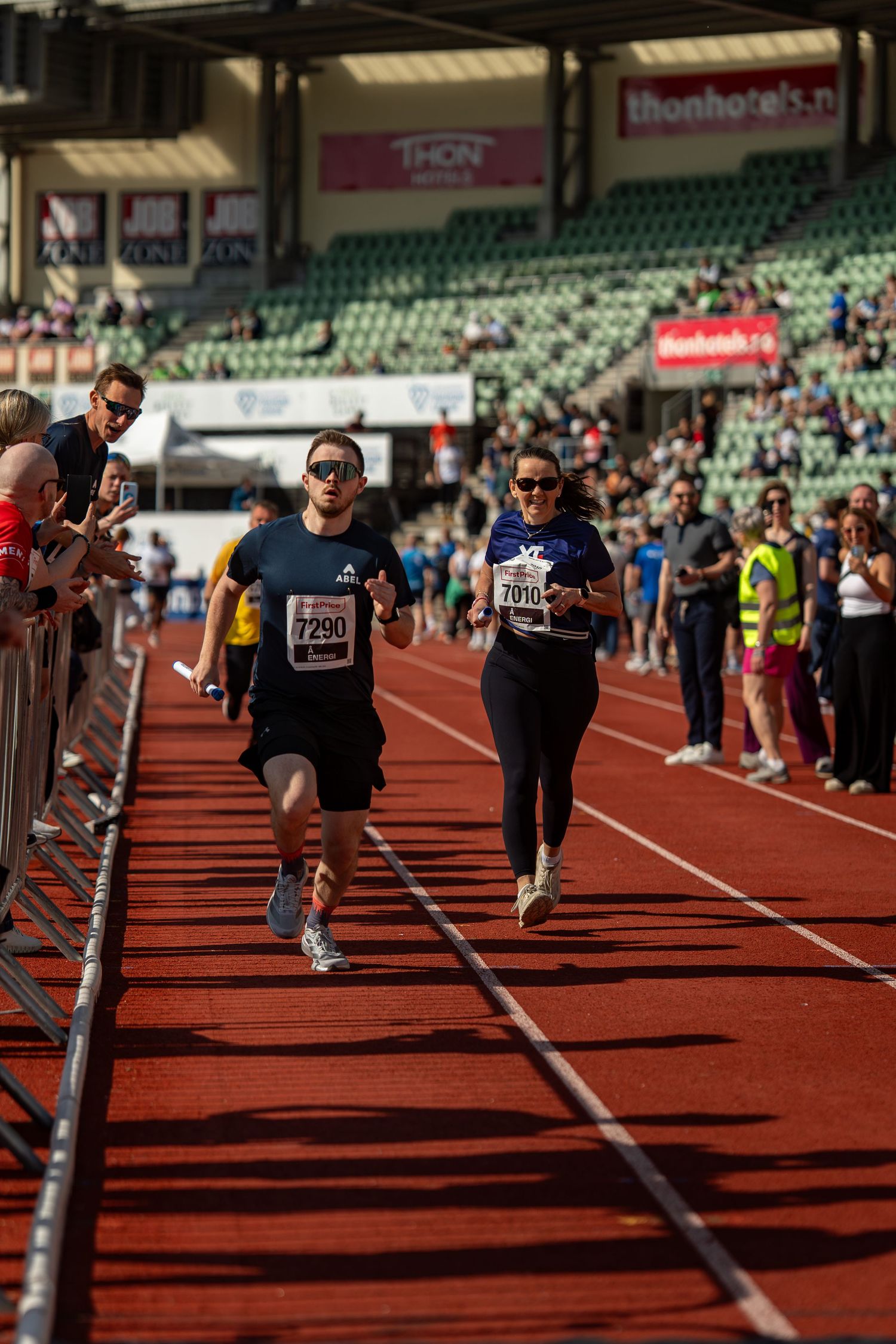 Athletes competing in a track race at a stadium with rows of empty green seats in the background.