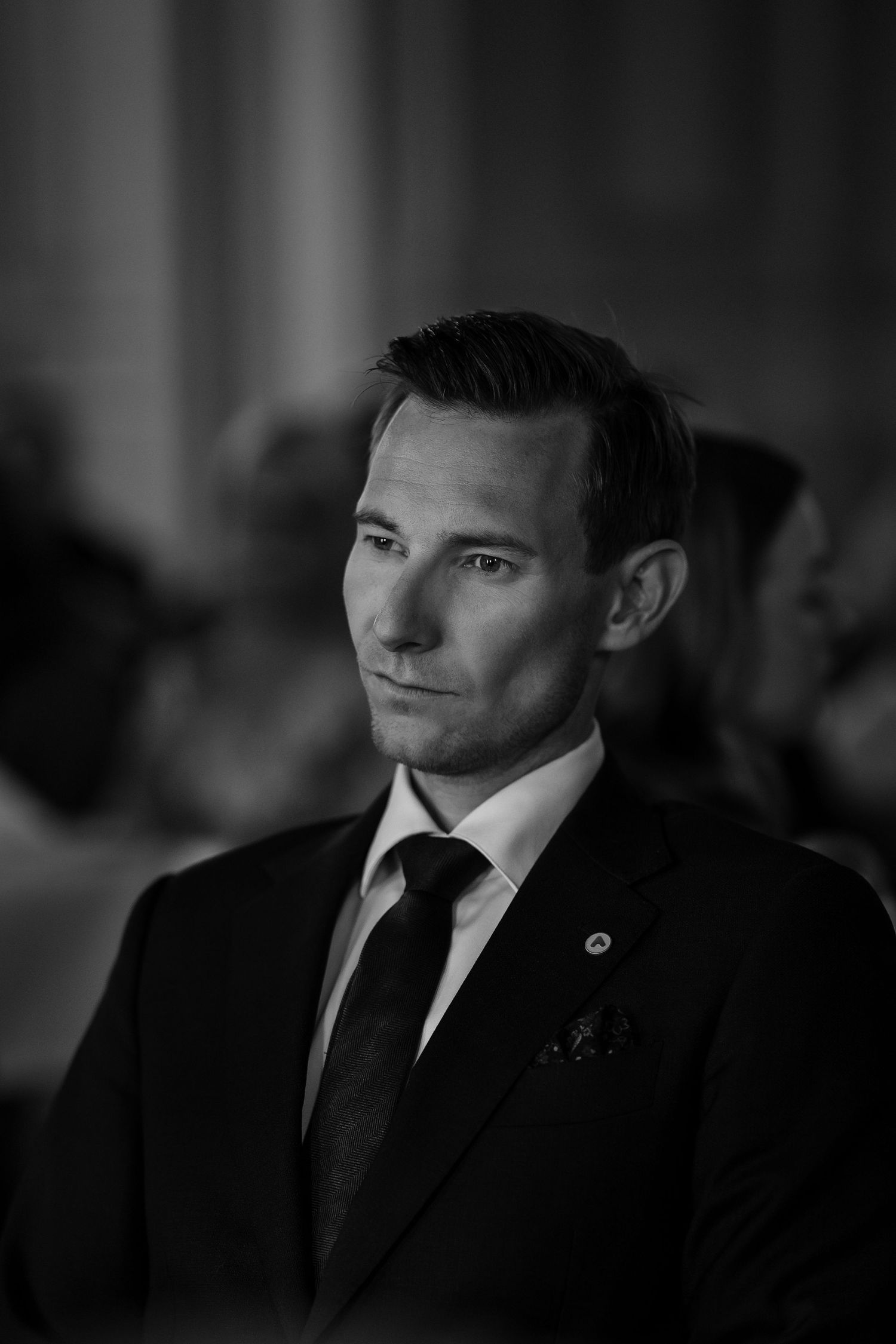 Man in dark suit smiles warmly during formal event in elegant setting.