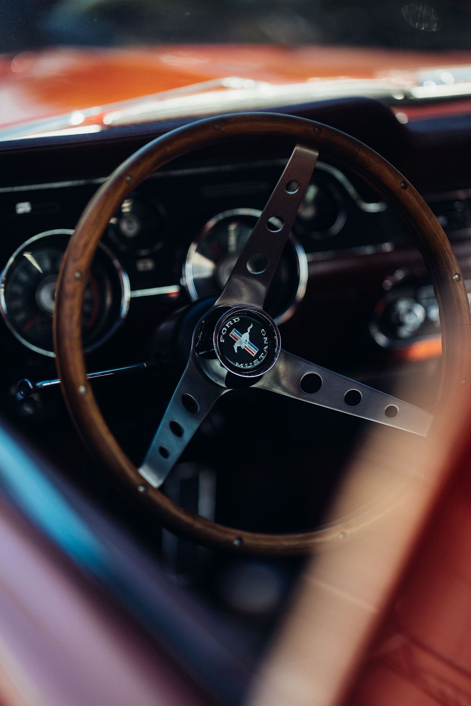 Classic wood steering wheel and dashboard gauges in vintage car interior.