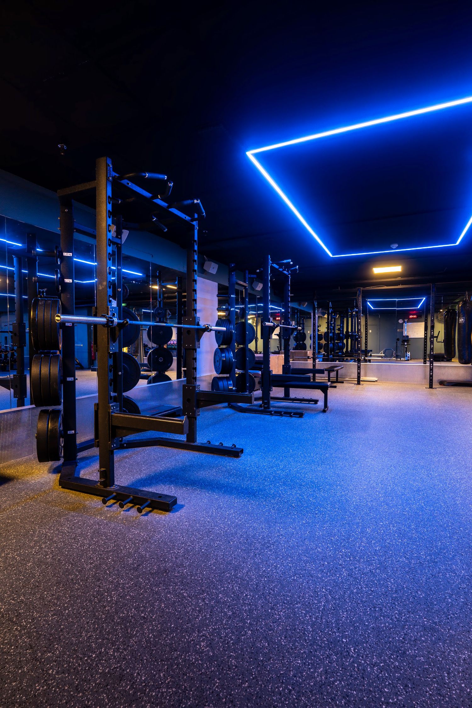 Weight training area with geometric blue LED ceiling lights and multiple squat racks.
