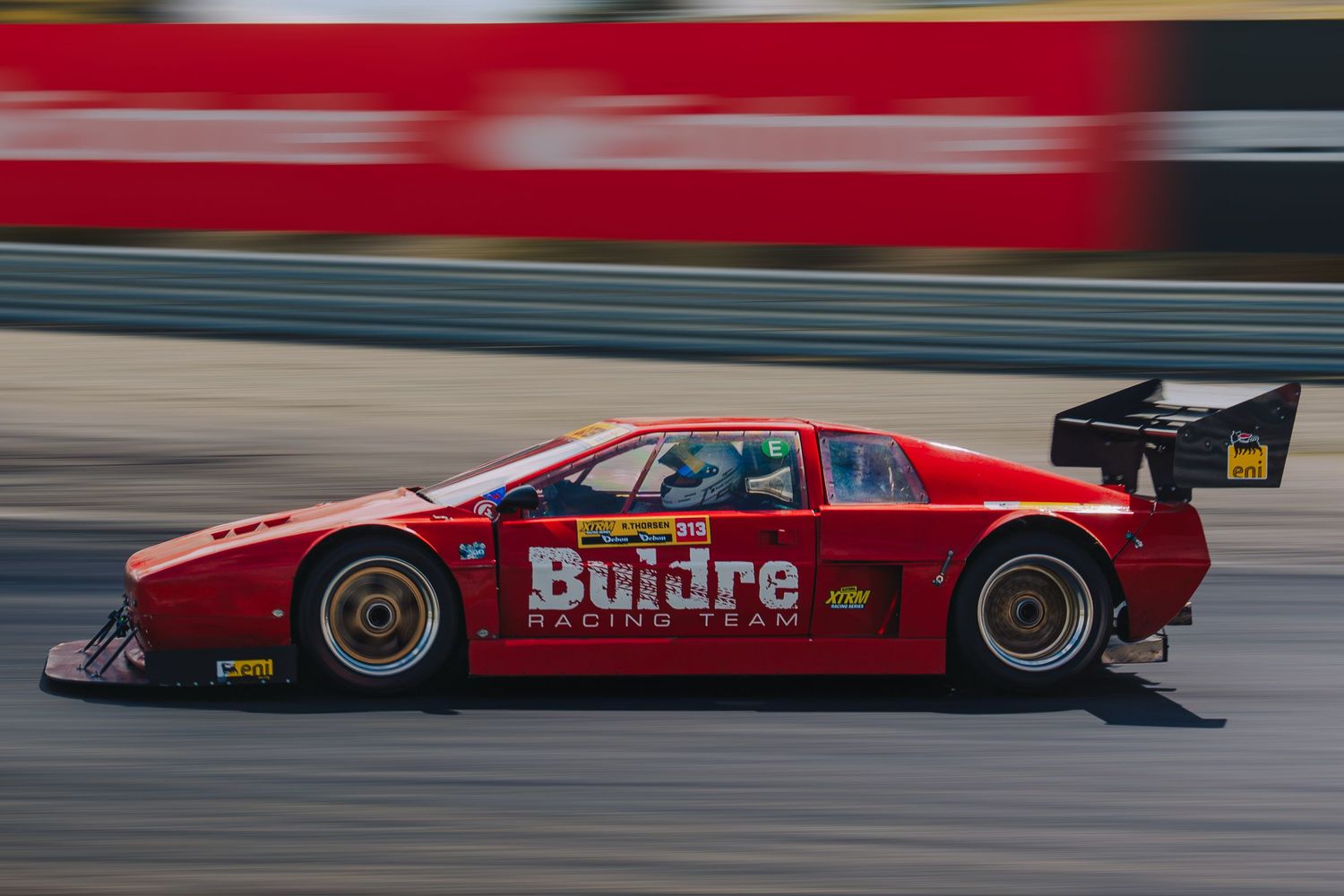 Red race car speeds down the track with motion blur creating a dynamic racing atmosphere.