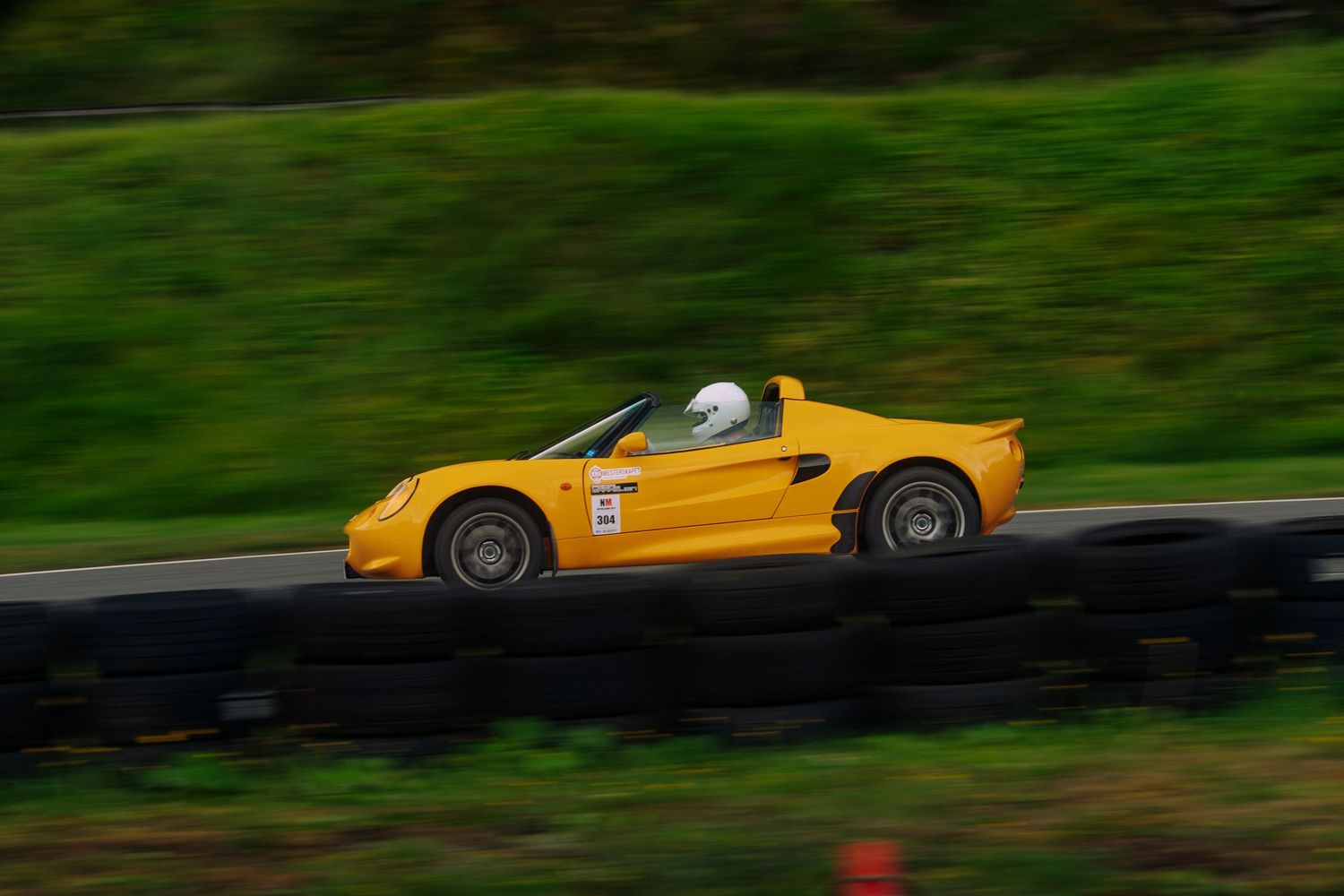 A bright yellow sports car speeds along a winding road through lush green scenery.