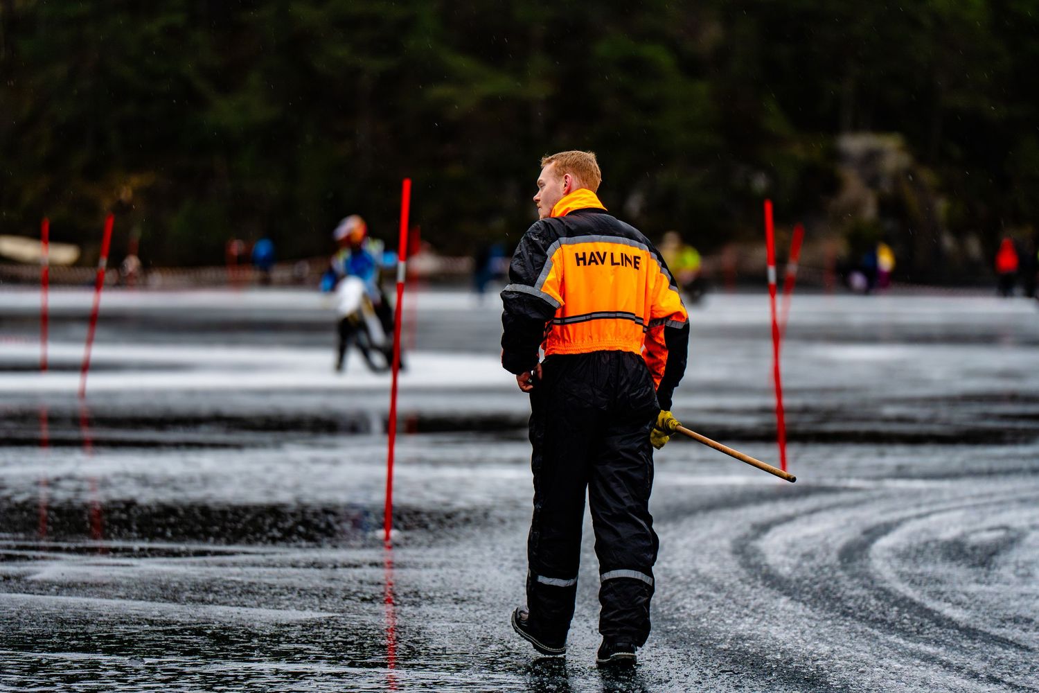 Safety personnel in reflective gear inspect a wet and icy road surface marked with red poles during winter conditions.