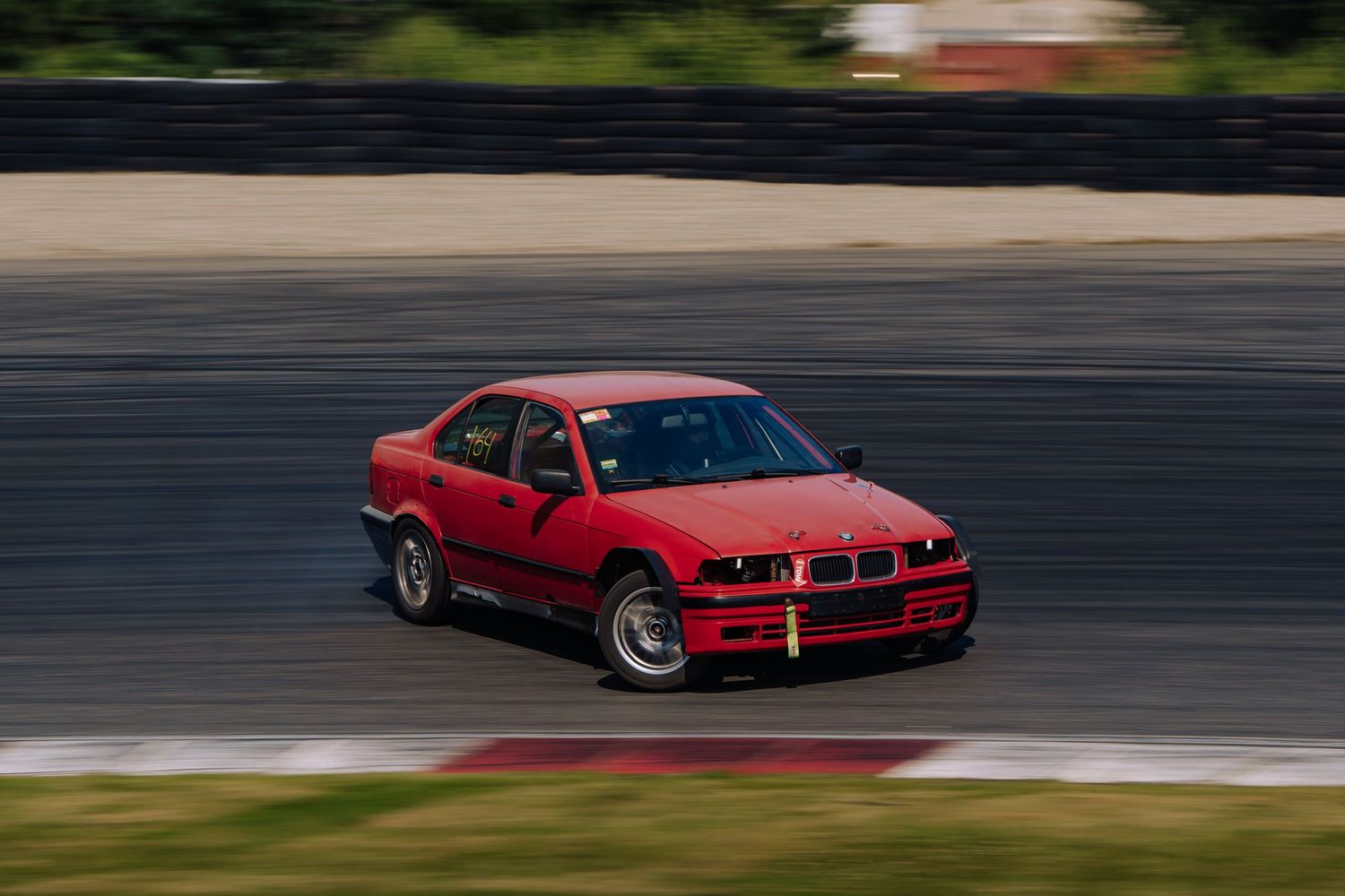 Red BMW E36 sports car drifting on a race track during a motorsport event.
