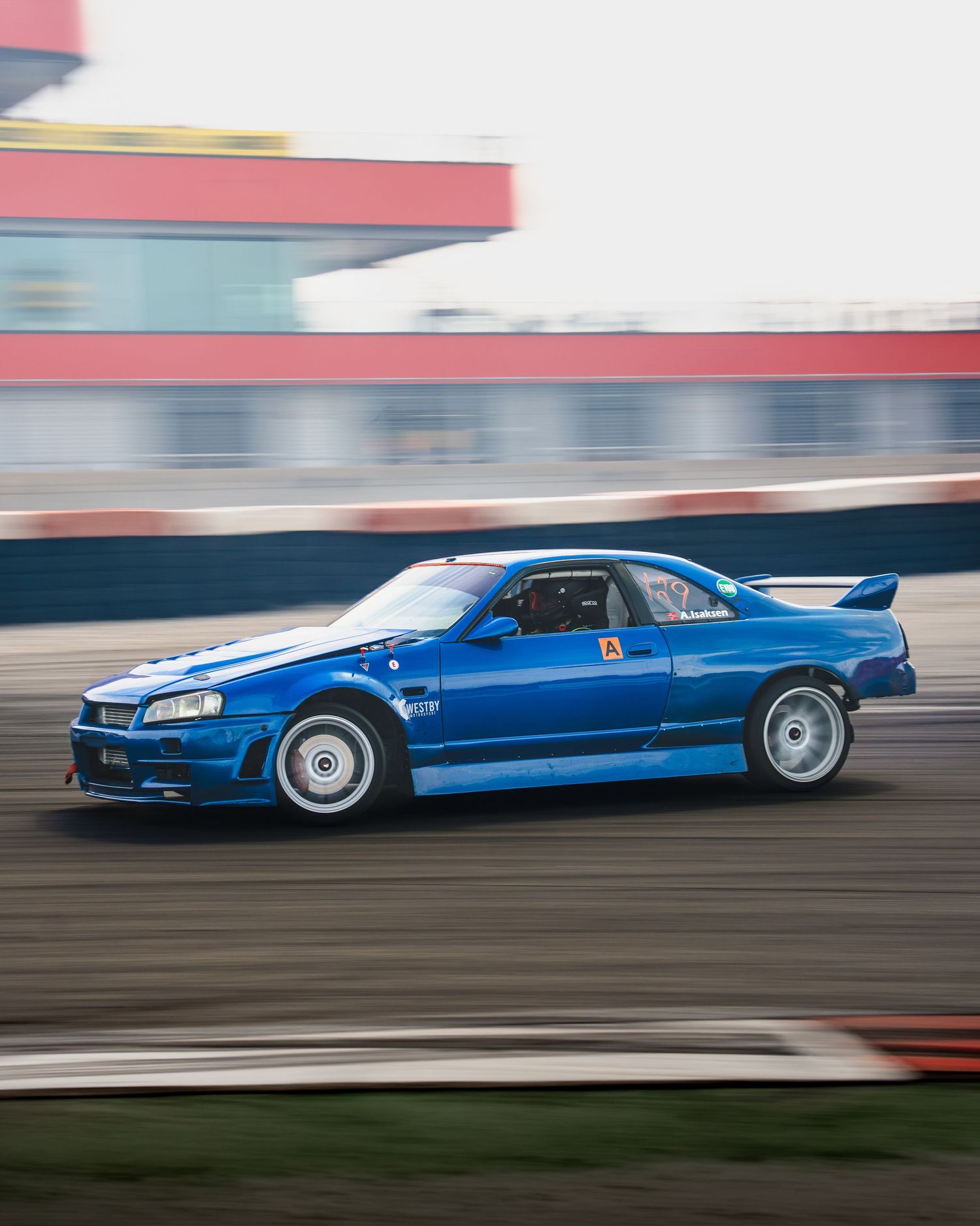 Blue Nissan Skyline R34 GT-R drifting on a race track with motion blur in the background.