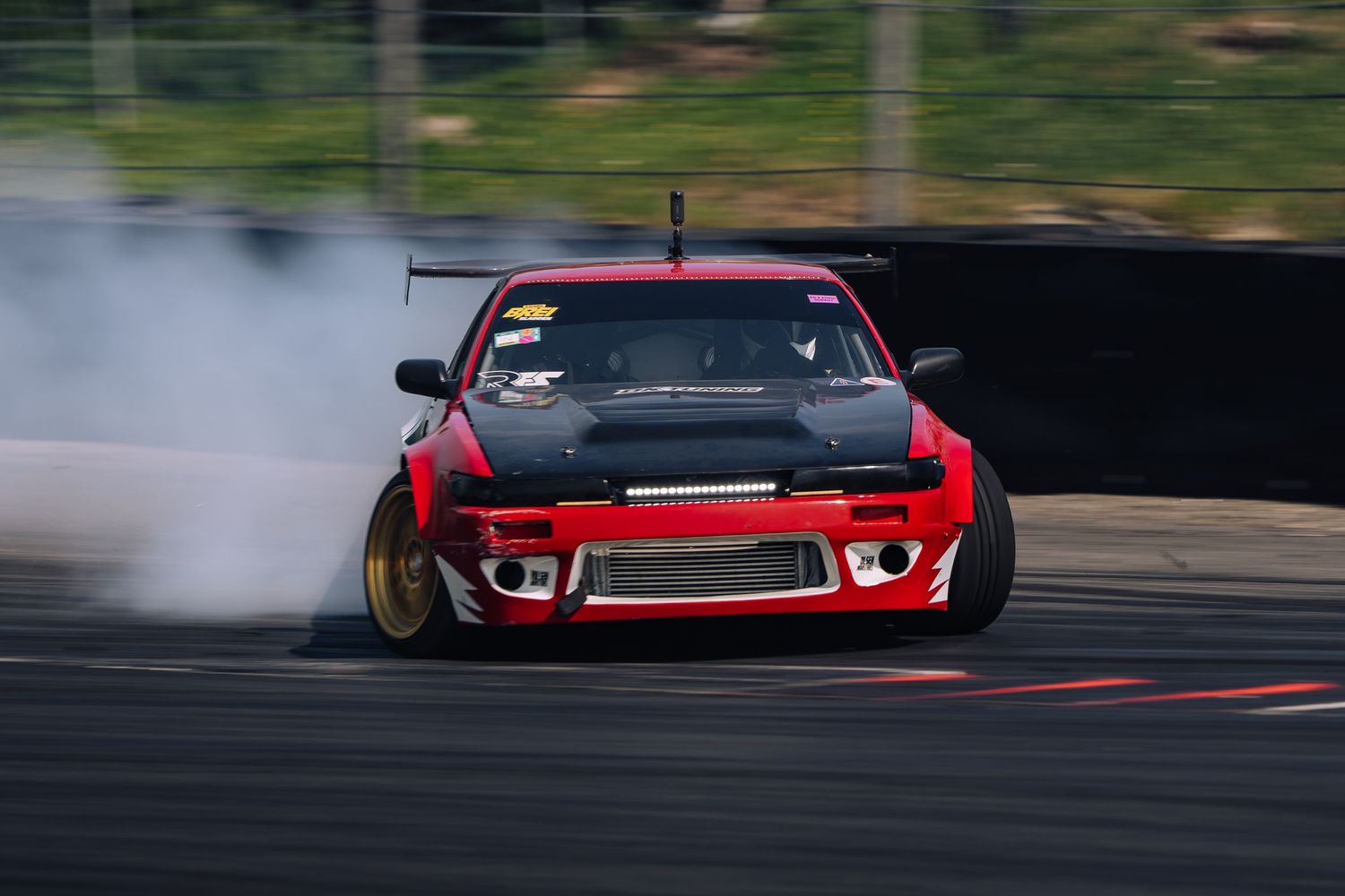 Red sports car drifting on a race track with smoke trailing behind during competitive motorsport action.