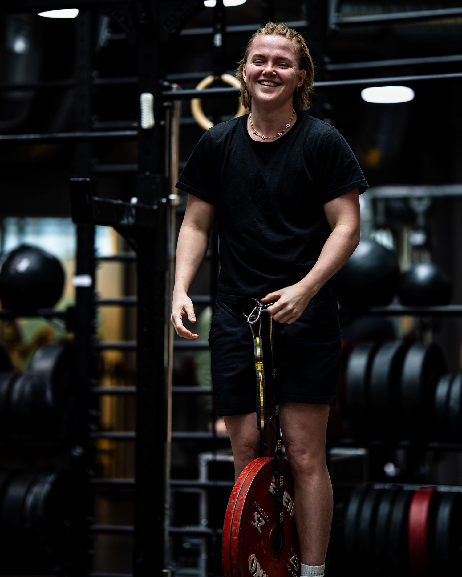 CrossFit athlete smiling in dark gym wearing black workout attire next to weight plates.