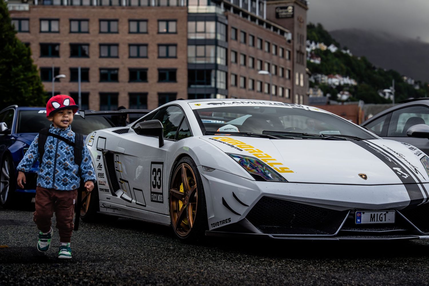 White Lamborghini Gallardo race car with gold wheels parked in front of brick building.