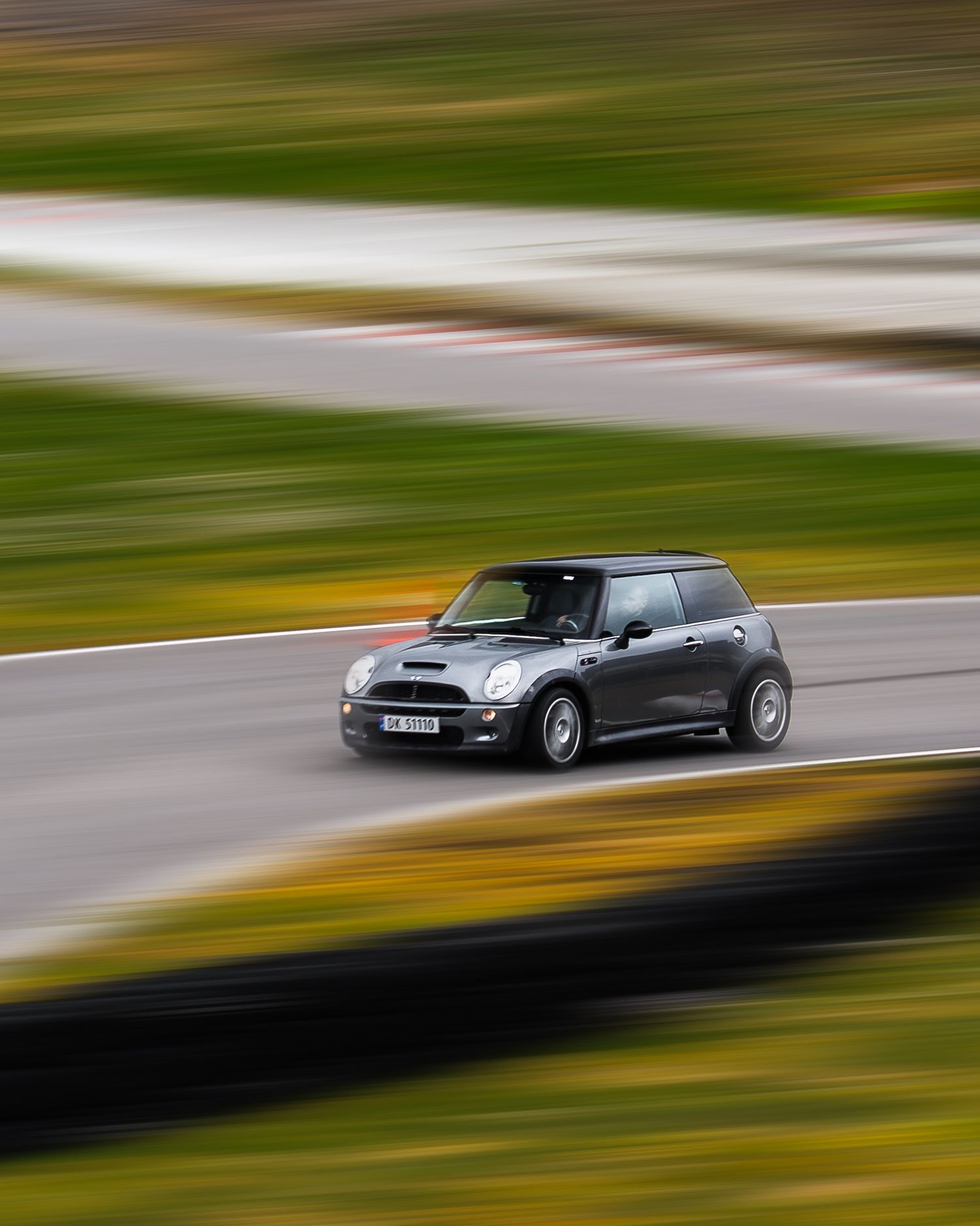 Motion blur photograph of three classic cars racing on a track with green scenery in the background.