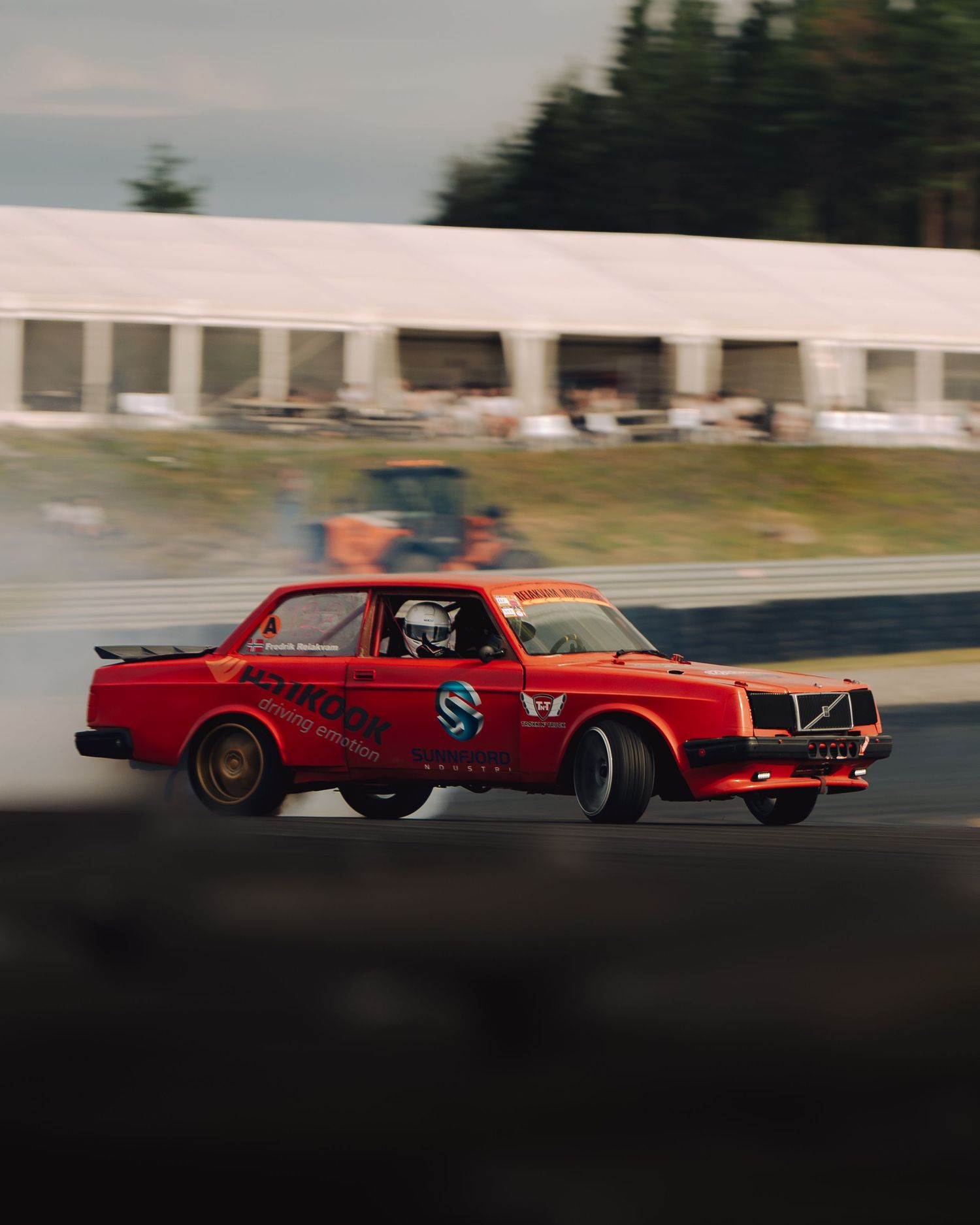 Red vintage race car speeding along a racetrack with motion blur effect creating a dynamic action shot.