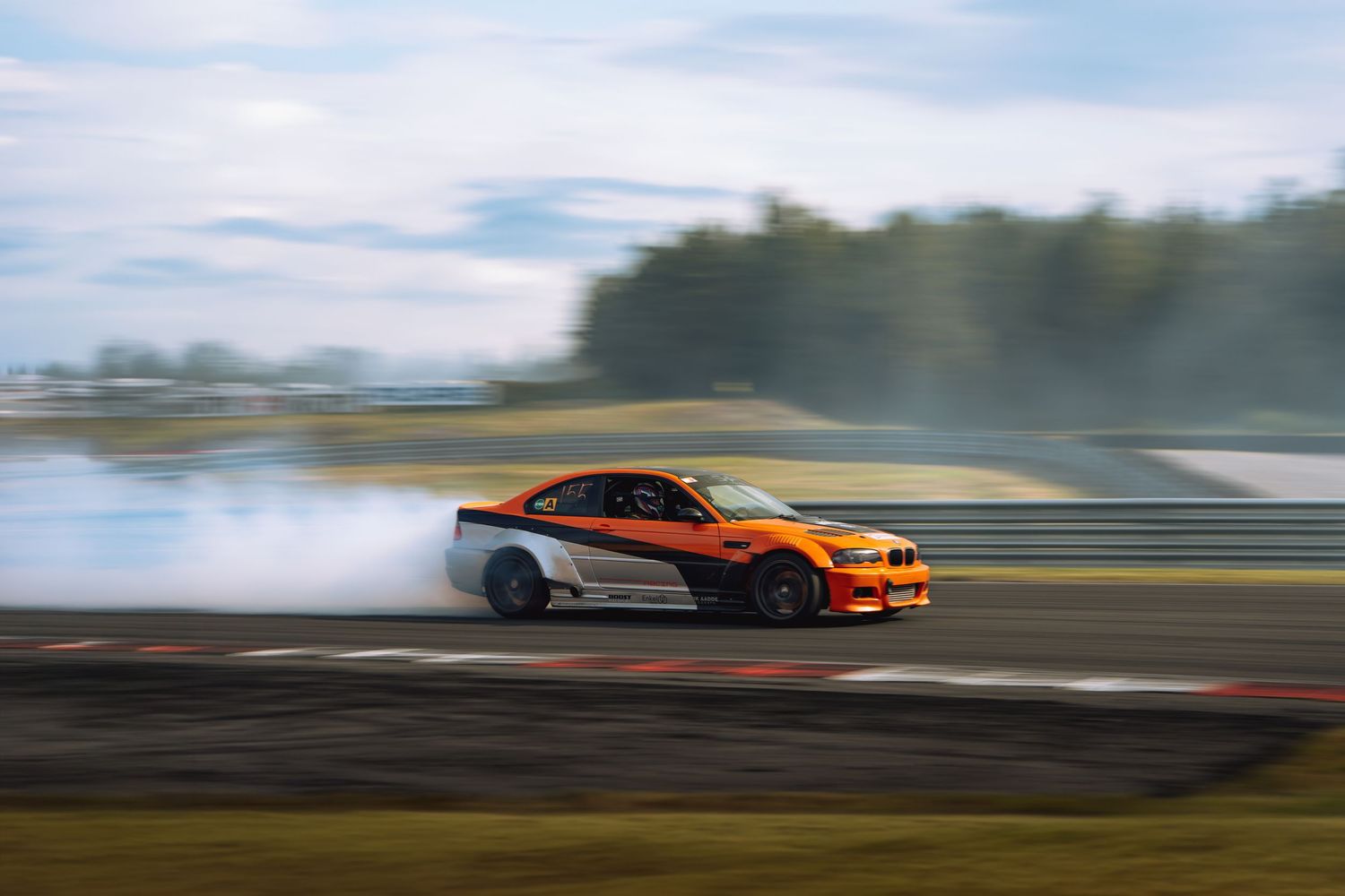 A silver and orange sports car drifting on a race track with motion blur effect and smoke from tires.