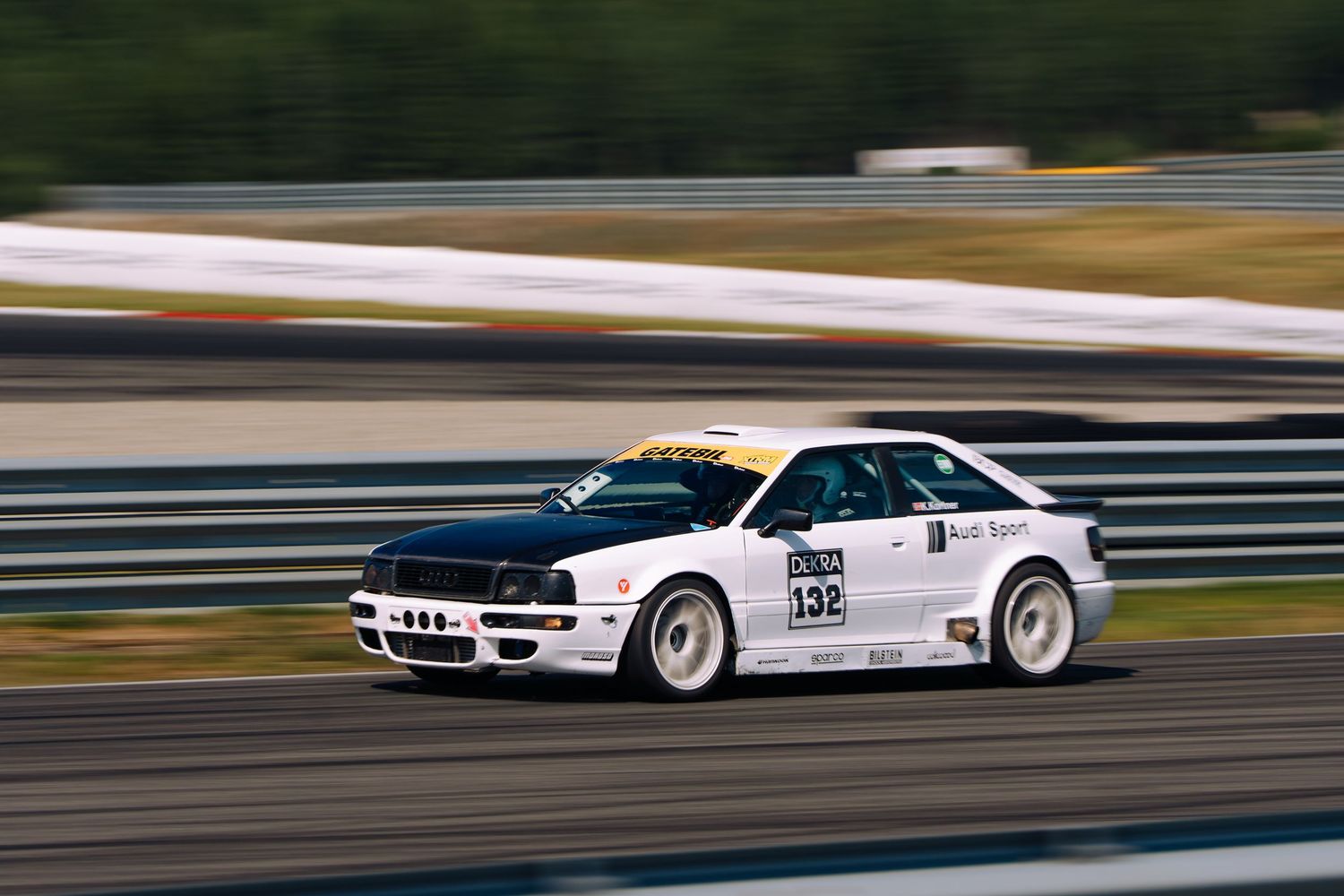 White race car speeds along track during motorsport competition showing motion blur effect.