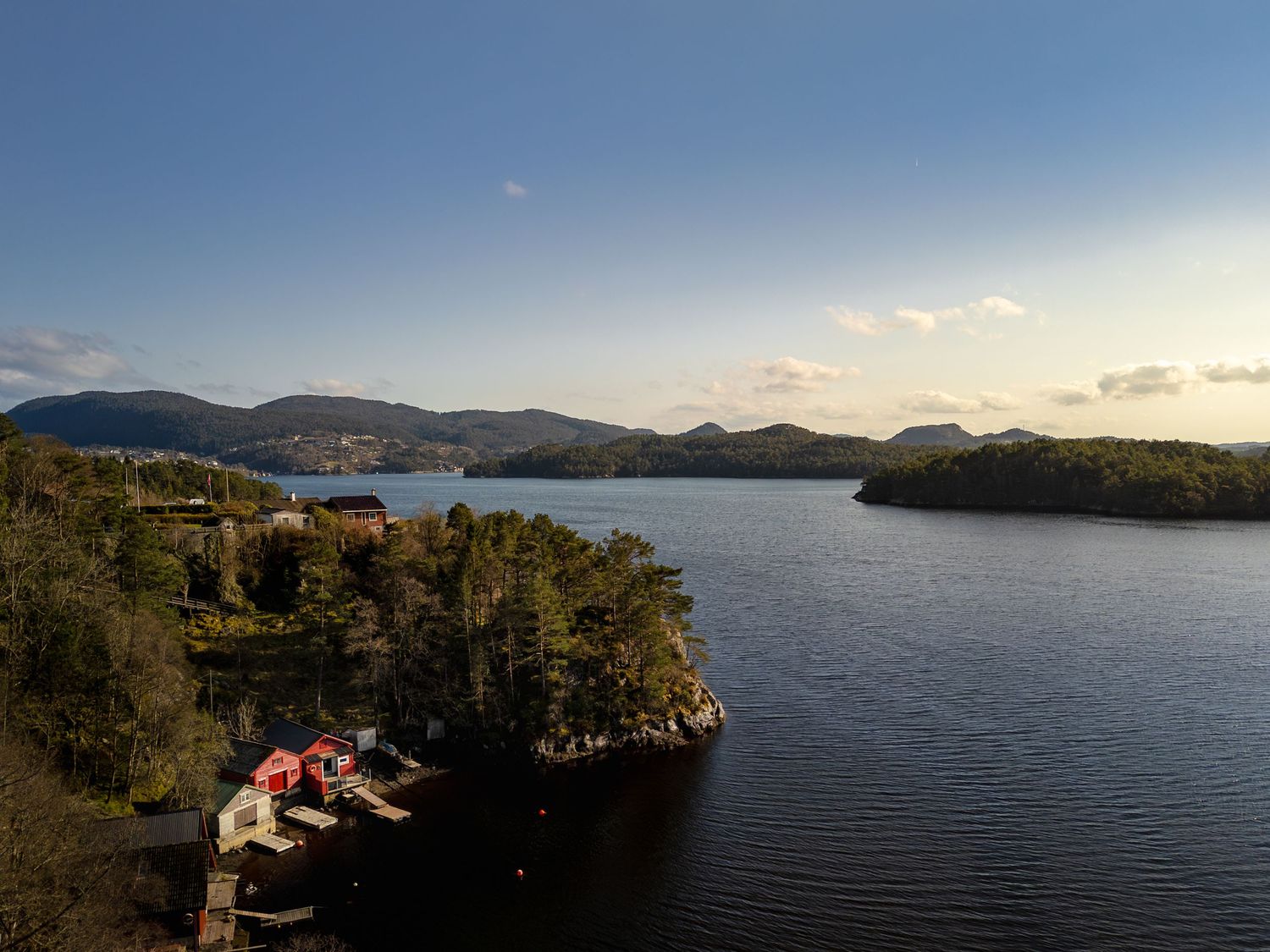 Panoramic view of a lake surrounded by mountains and forests at sunset.