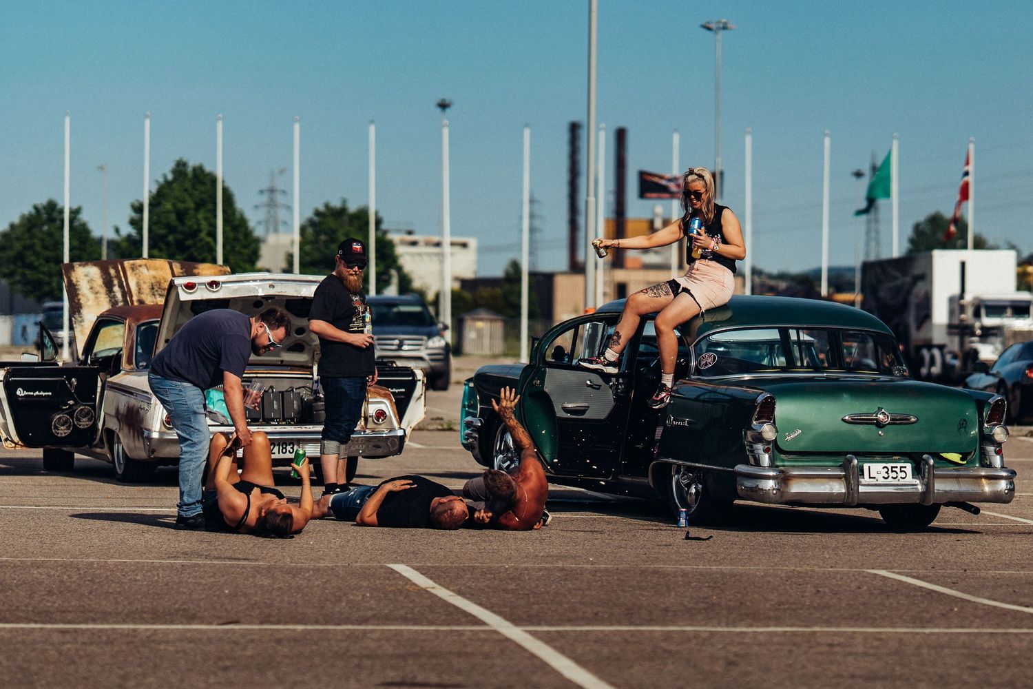 Vintage cars and casual gathering in parking lot on sunny summer day.