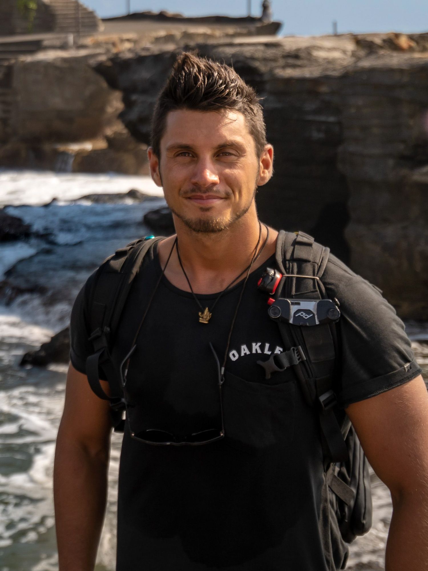 Person in black t-shirt and backpack exploring rocky coastal terrain.