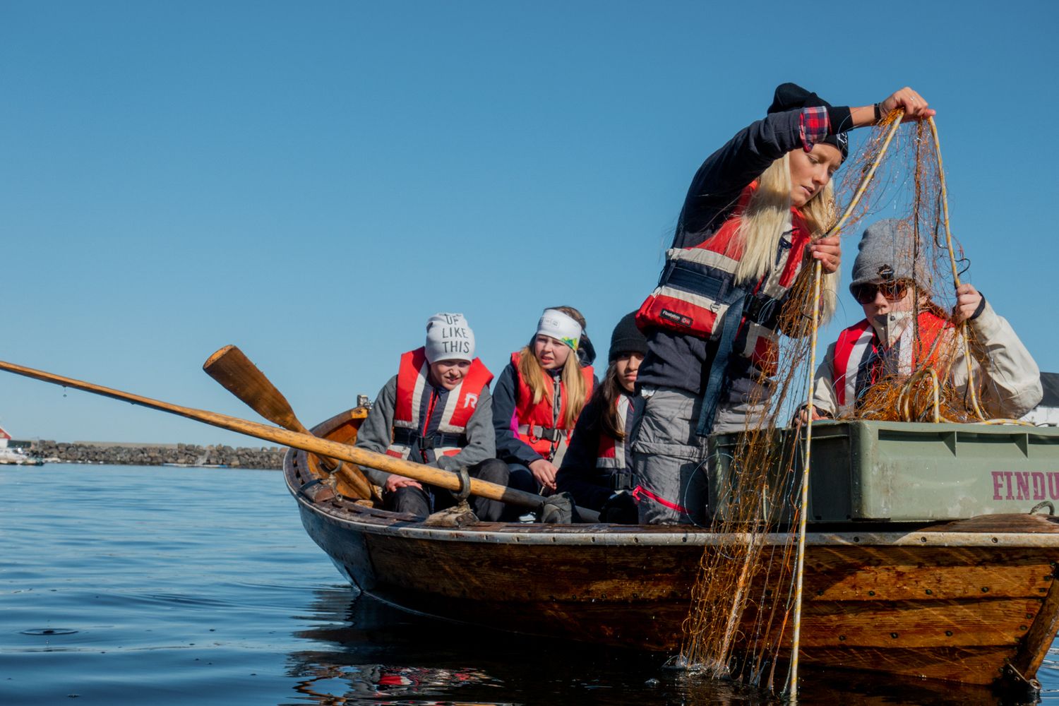 Traditional wooden boat with crew members handling fishing nets on calm waters.