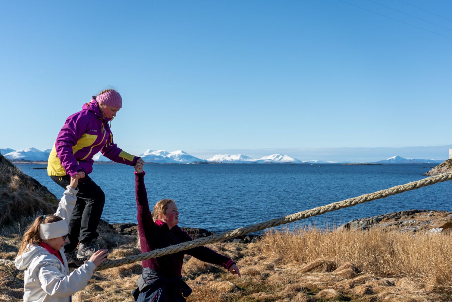 Adventure seekers explore the rugged coastal terrain with snowy mountains in the background.